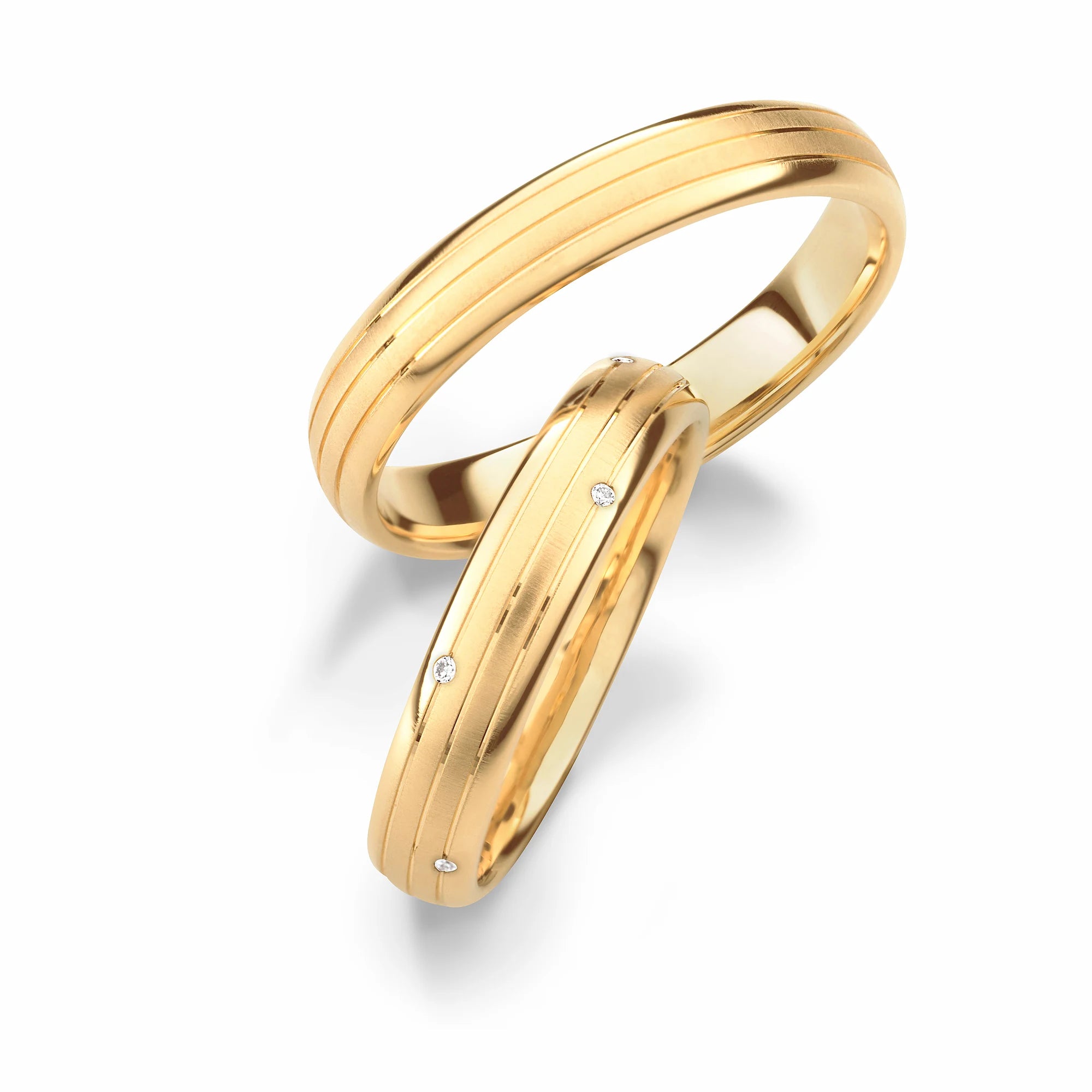 Produktfotografie des gelbgoldenen Max Kemper Trauringpaars mit 3 feinen eingravierten Linien, die sich um den Ring herumziehen und Diamanten als Verzierung für den Damenring