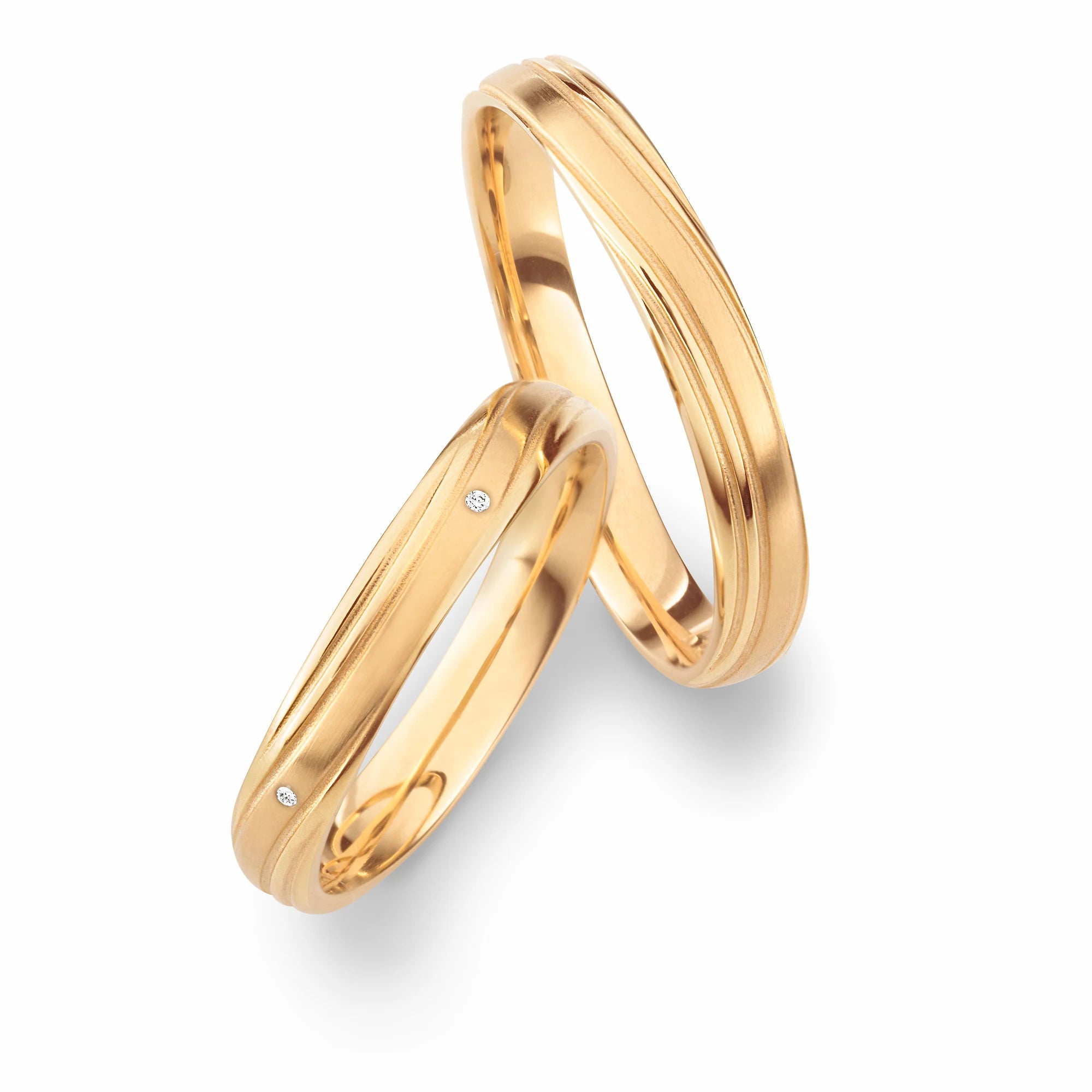 Produktfotografie des gelbgoldenen Max Kemper Trauringpaars mit fliesend angeordneten Linien auf der Oberfläche und mit Diamanten im Damenring