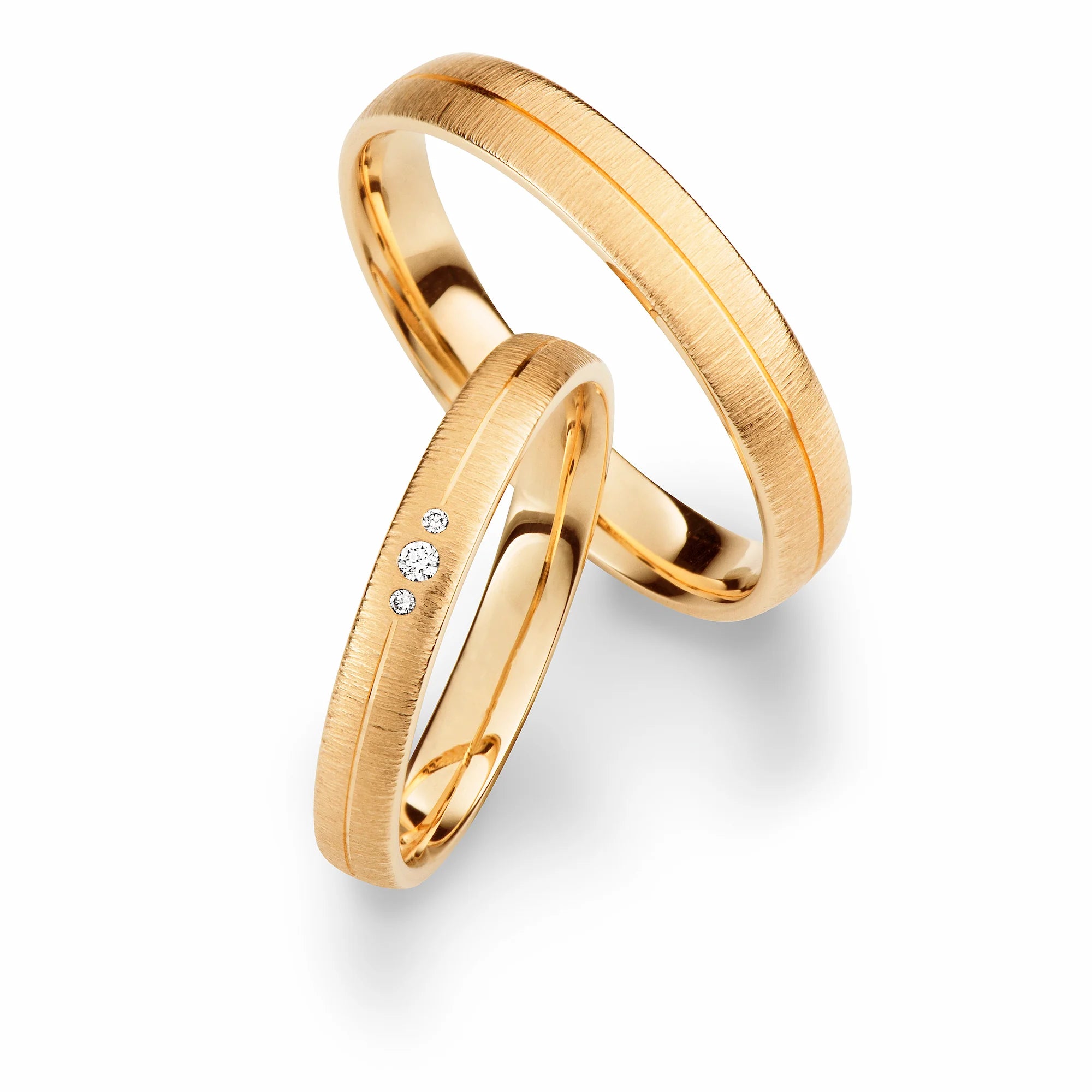 Produktfotografie des gelbgoldenen Max Kemper Trauringpaars mit Borke-Oberfläche und einer zentralen, durchgezogenen polierten Phase und 3 Diamanten im Damenring