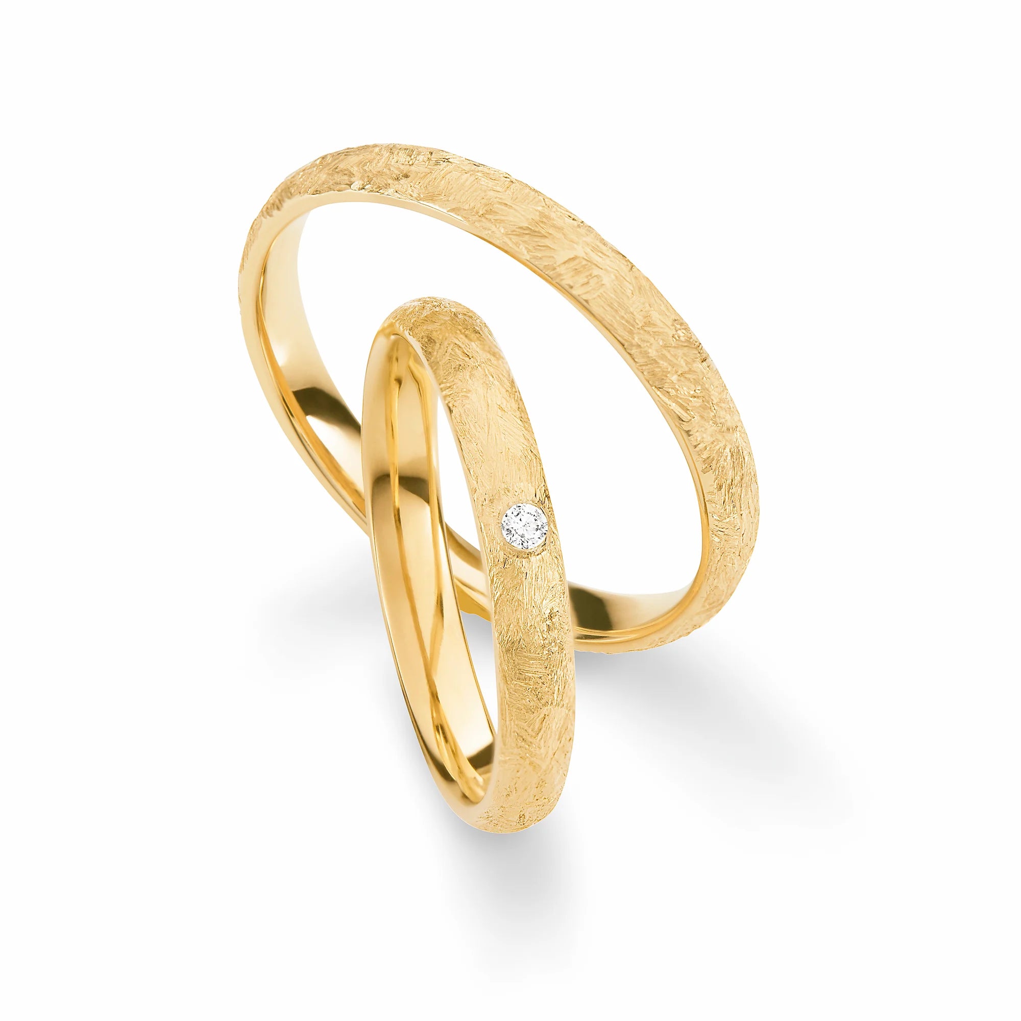 Produktfotografie des gelbgoldenen Max Kemper Trauringpaars mit wild gebürsteter Oberflächenstruktur und einem zentralen Diamant als Verzierung des Damenrings