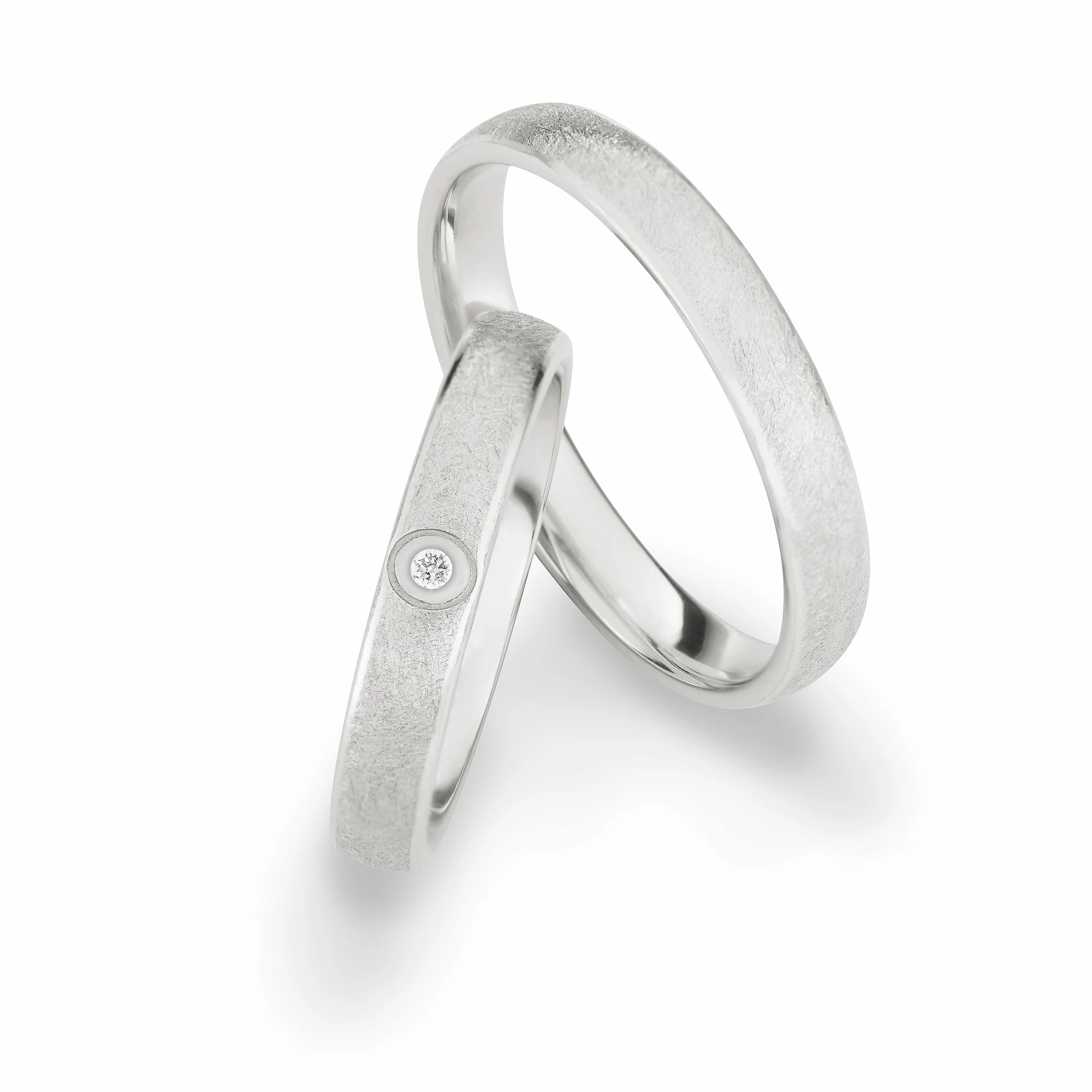 Produktfotografie des weissgoldenen Max Kemper Trauringpaars mit "Frosted"-Oberflächenstruktur und einem zentralen Diamanten als Verzierung des Damenrings