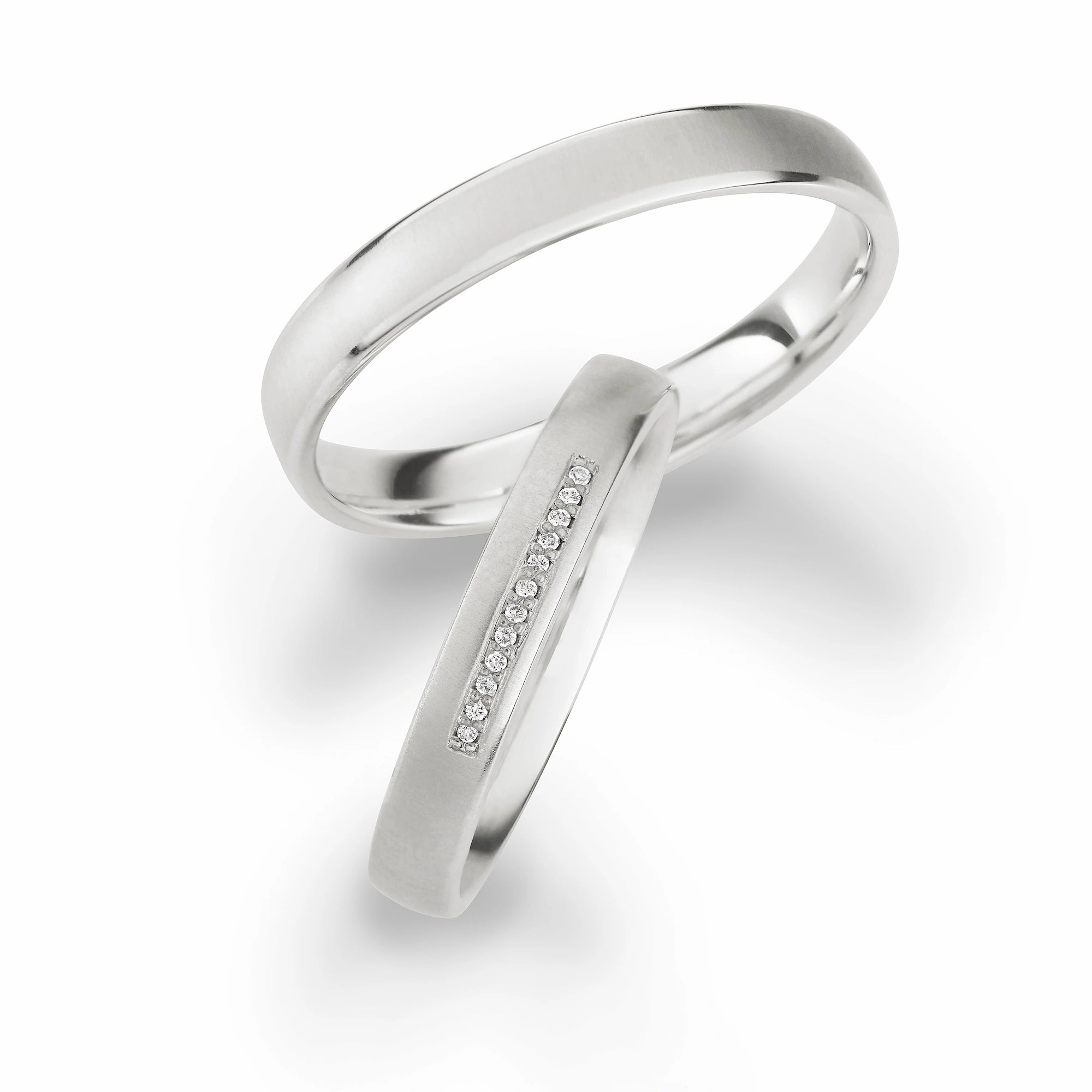 Produktfotografie des weissgoldenen Max Kemper Trauringpaars mit fein gebürsteter Oberflächenstruktur und einer Diamant-Reihe aus 12-Brillanten als Verzierung des Damenrings