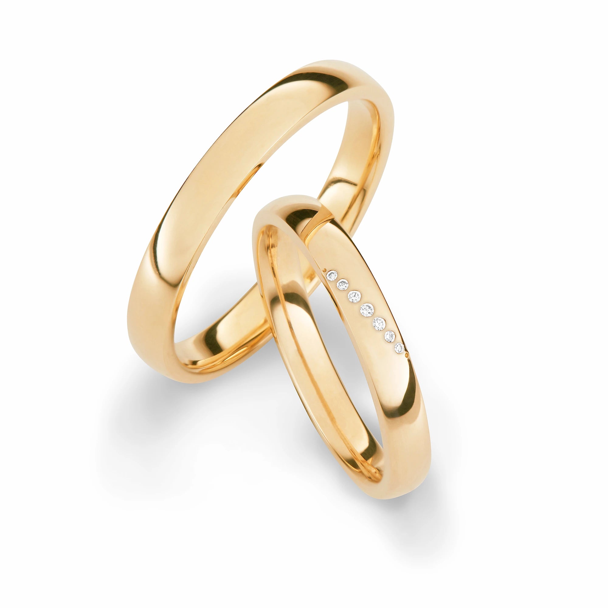 Produktfotografie des gelbgoldenen Max Kemper Trauringpaars mit polierter Oberfläche und einer schräg platzierten Diamant-Reihe aus 7 Brillanten auf dem Damenring