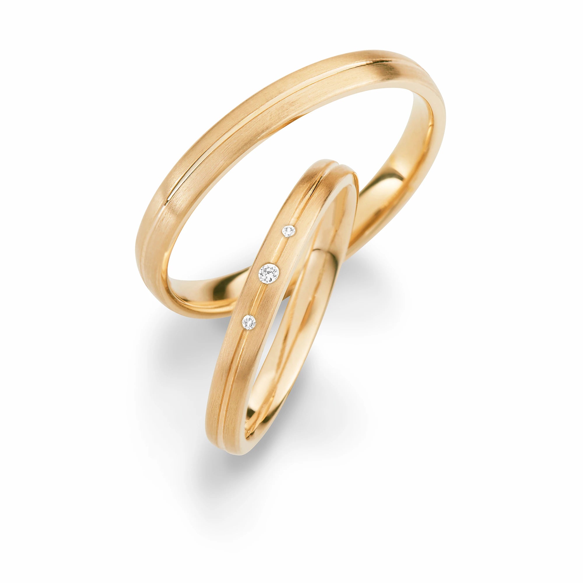 Produktfotografie des gelbgoldenen Max Kemper Trauringpaars mit längst gebürsteter Oberflächenstruktur und einer zentralen, polierten Nut, sowie drei Diamanten als Verzierung des Damenrings