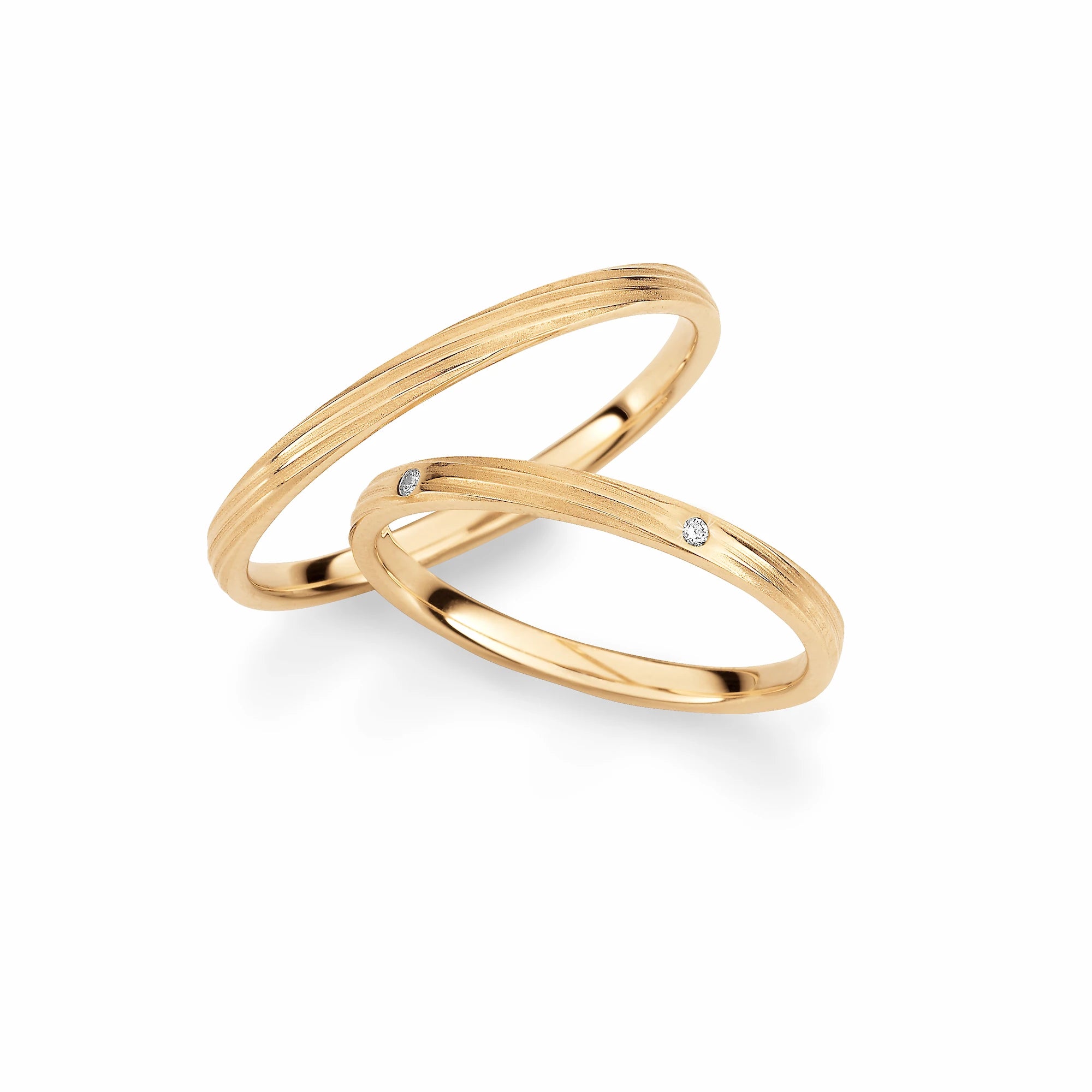 Produktfotografie des gelbgoldenen Max Kemper Trauringpaars mit geschwungenen, um den Ring herumlaufenden Linien und Diamanten im Damenring