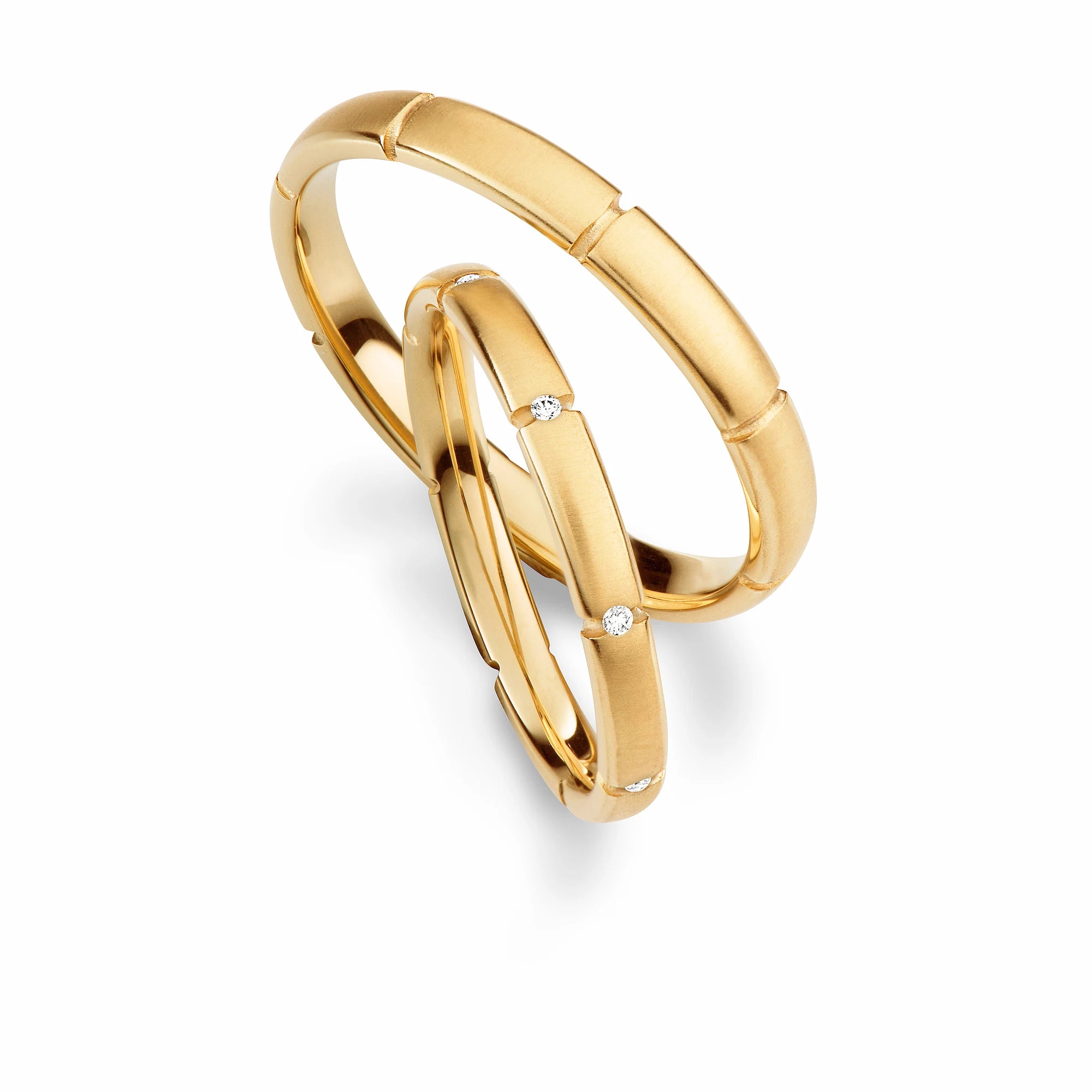 Produktfotografie des gelbgoldenen Max Kemper Trauringpaars mit einer fein strukturierten Oberfläche und sich regelmäßig wiederholenden Einkerbungen in der Ringschiene und in den Einkerbungen eingesetzten Diamanten im Damenring