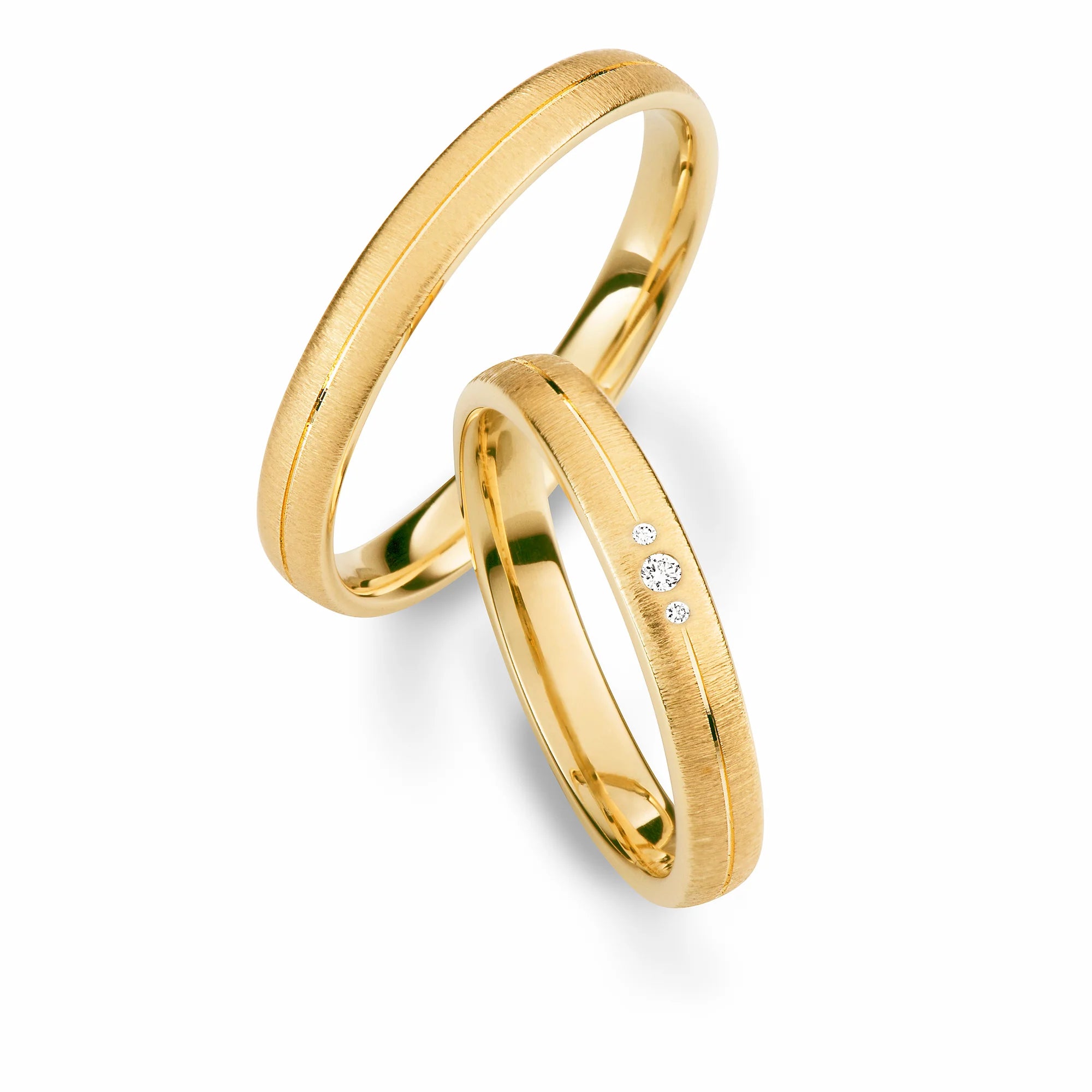 Produktfotografie des gelbgoldenen Max Kemper Trauringpaars mit einer quer gebürsteten Oberflächenstruktur und einer zentral eingelassenen, glänzenden Nut und 3 Diamanten im Damenring