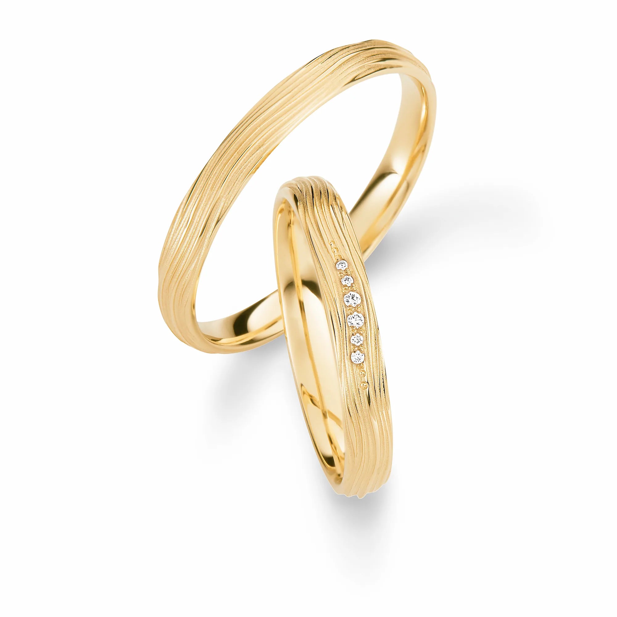 Produktfotografie des gelbgoldenen Max Kemper Trauringpaars mit einer strukturierten wellenförmigen Oberfläche  und vereinzelten Diamanten im Damenring