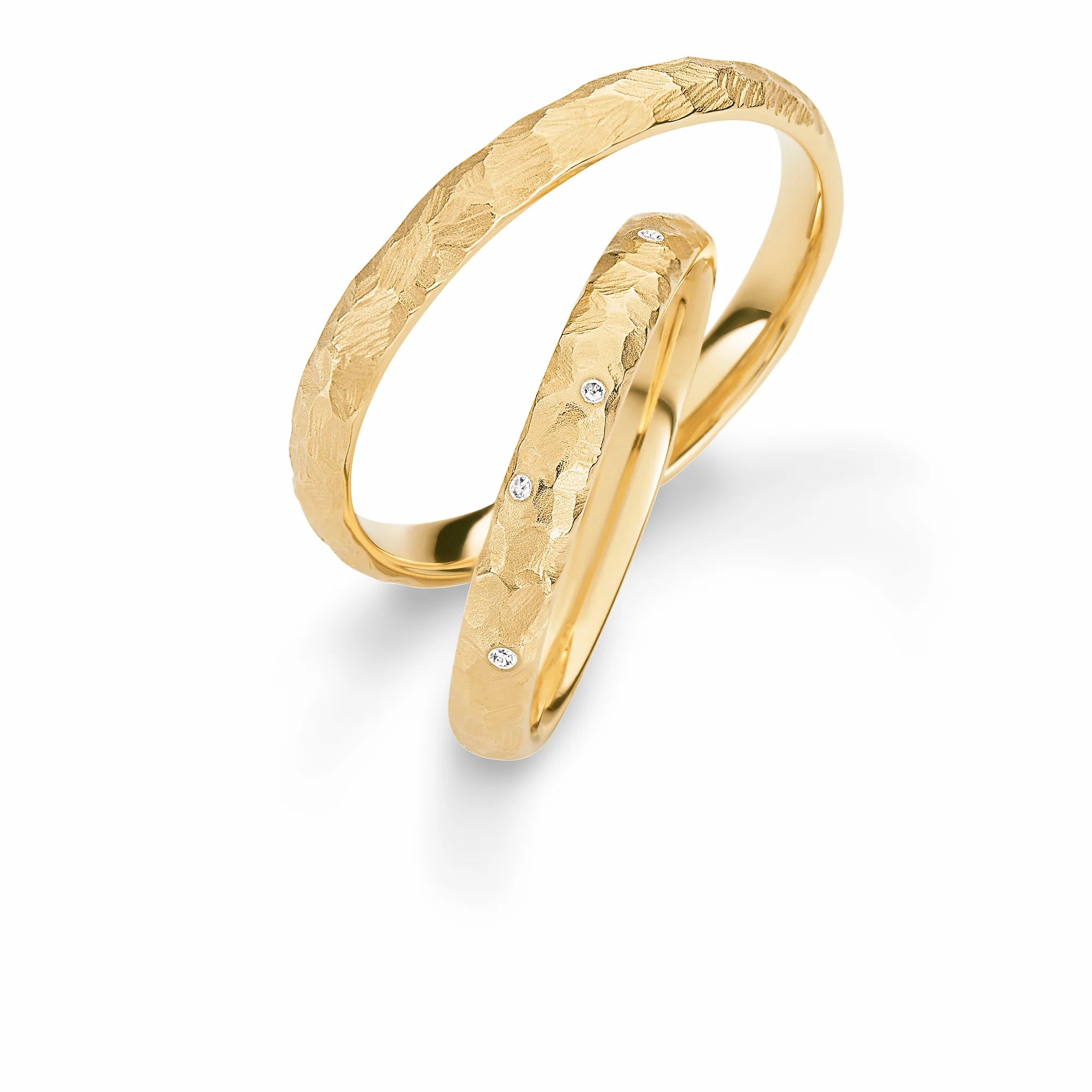 Produktfotografie des gelbgoldenen Max Kemper Trauringpaars mit einer strukturierten Oberfläche mit grobem Hammerschlag und vereinzelten Diamanten im Damenring