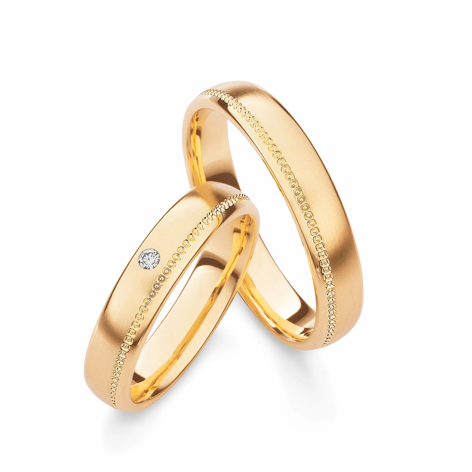 Produktfotografie des gelbgoldenen Max Kemper Trauringpaars mit einer fein strukturierten Oberflächenstruktur und einer leicht versetzt laufenden Zier-Nut bestehend aus einzelnen Kringeln im und einem zentralen Diamanten im Damenring