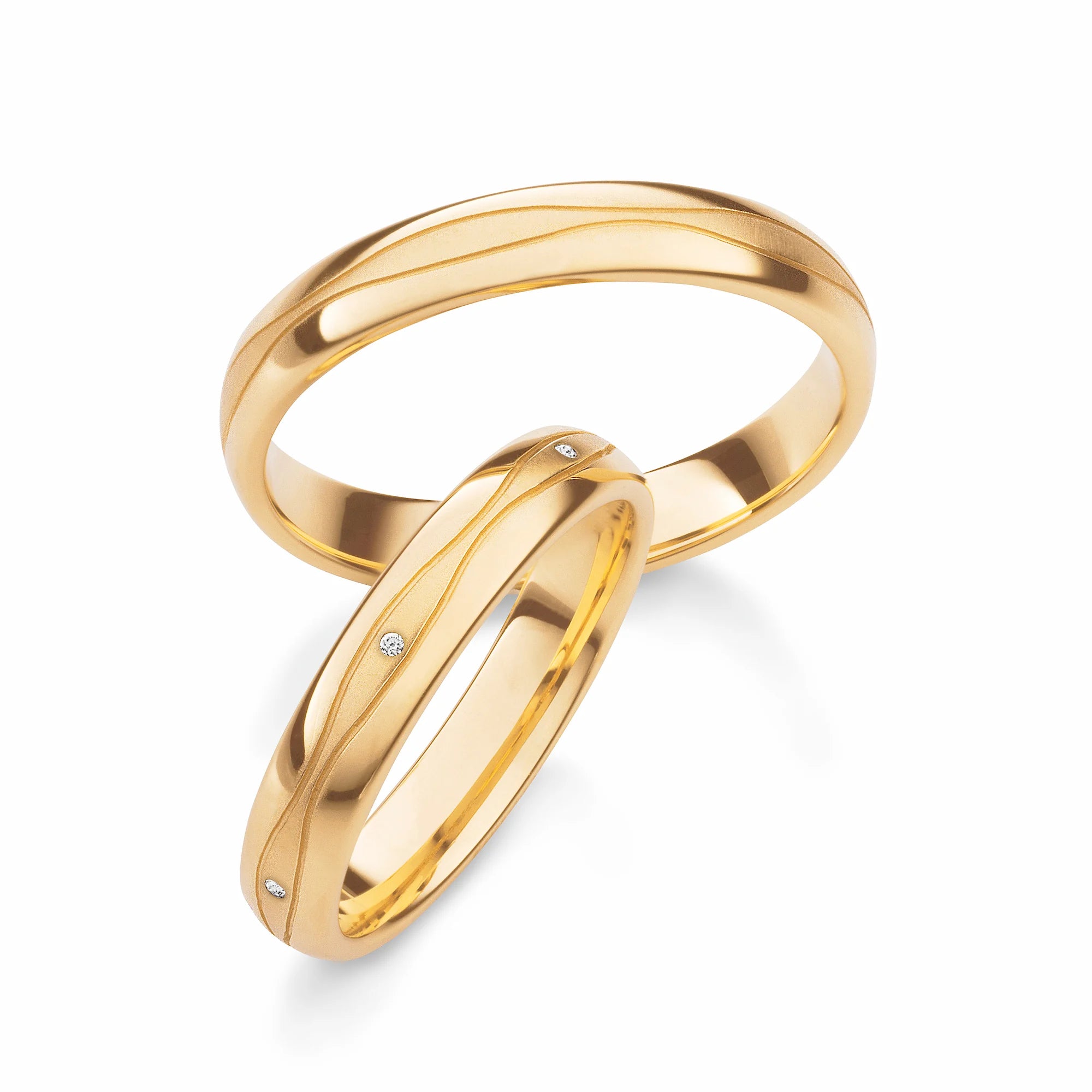 Produktfotografie des gelbgoldenen Max Kemper Trauringpaars mit einer polierten Oberflächenstruktur und zwei organisch verlaufenden, eingravierten Nuten und  Diamanten im Damenring