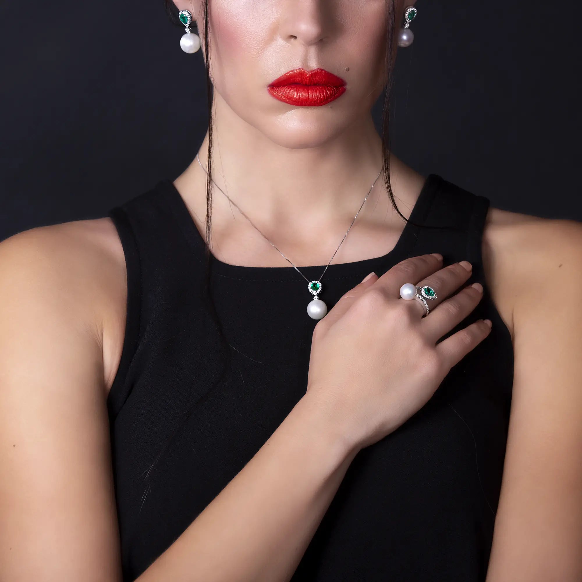 Model mit roten Lippen trägt das Schmuckset mit Ohrsteckern, einem Collier und Ring von Lunatica Roma welches durch Perlen, Smaragde und Brillanten verziert ist