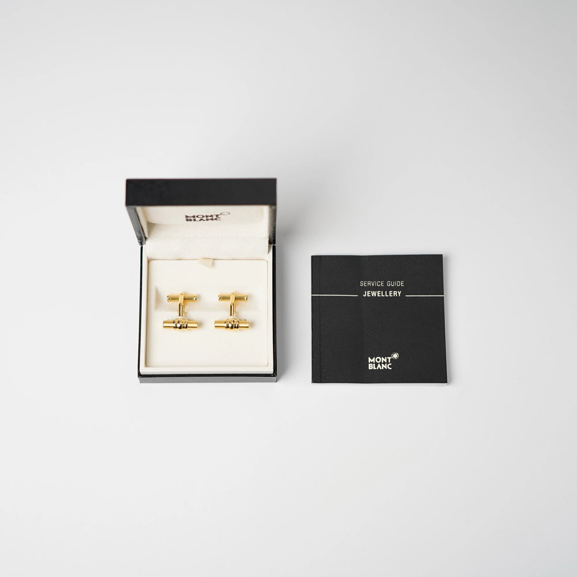 Gold-plattinierte Manschettenknöpfe von Mont Blanc mit der Modellbezeichnung "Bar 3 Rings" liegen in der originalen Schachtel und daneben der Jewellry Service Guide der Marke