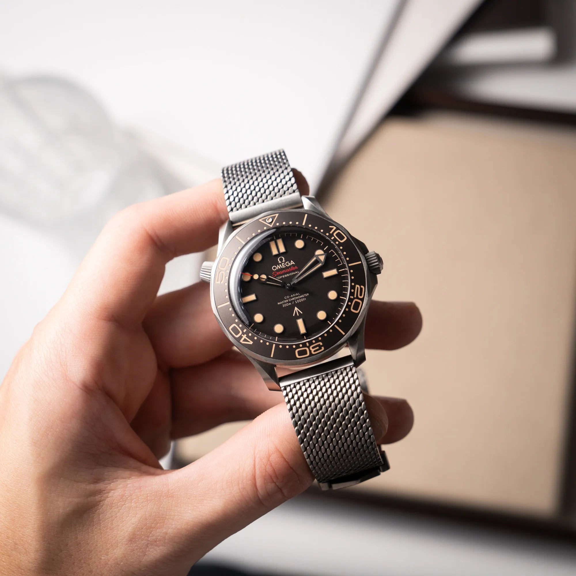 Mann hält die Omega Seamaster 300m Diver No Time To Die Limited Edition aus Titan mit braunem Zifferblatt und präsentiert die Uhr in die Kamera