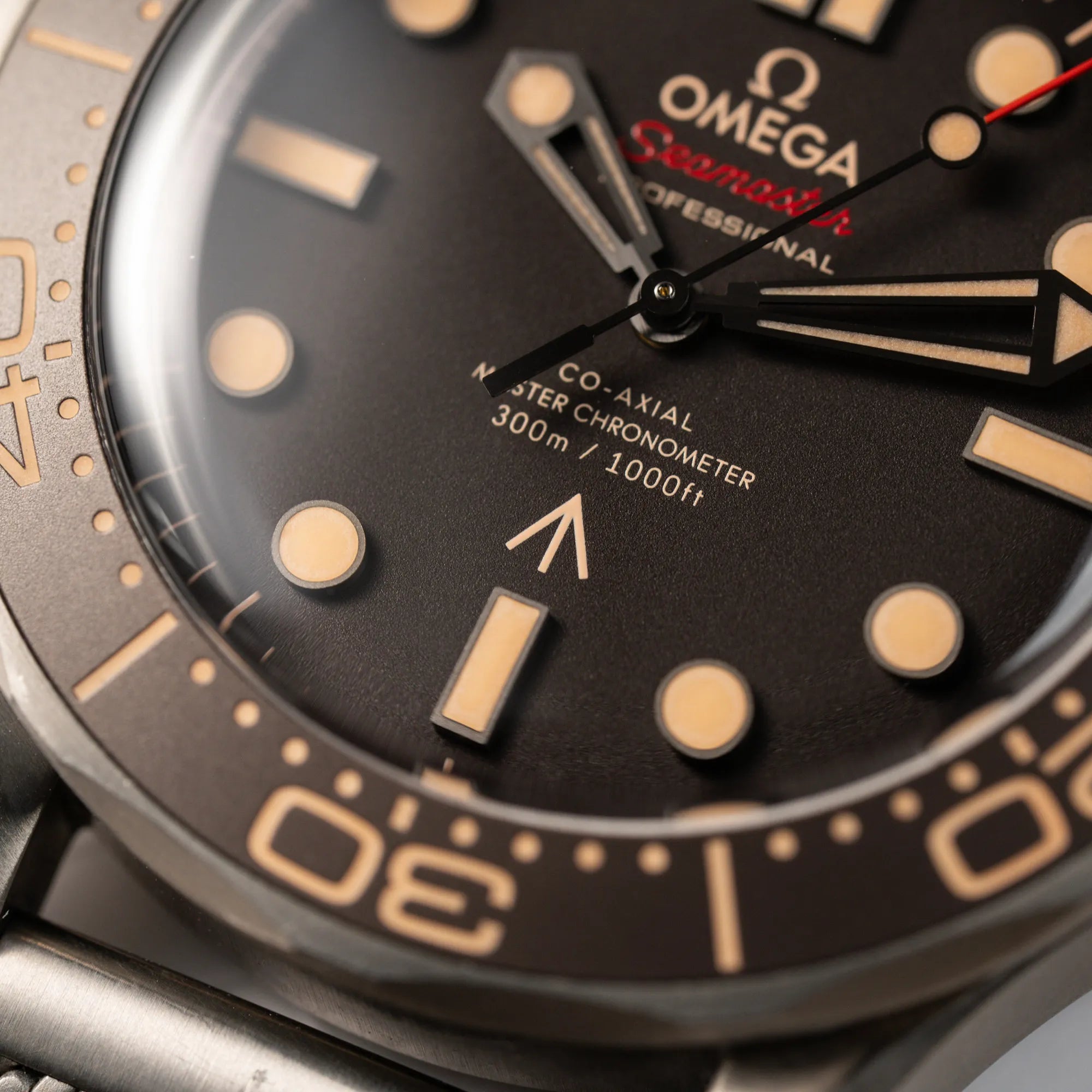 Makroaufnahme der Omega Seamaster 300m Diver No Time To Die Limited Edition aus Titan mit braunem Zifferblatt mit Fokus auf dem "Co-Axial Master Chronometer" Schriftzug auf dem Zifferblatt