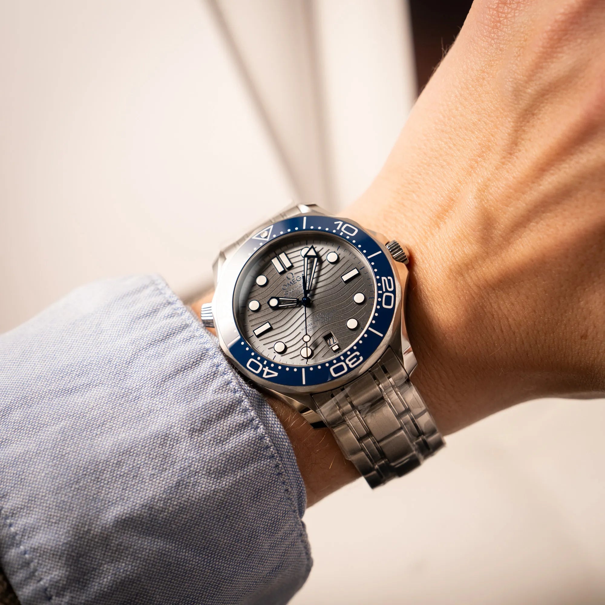 Wristshot mit der Omega Seamaster Diver 300M der Referenz 210.30.42.20.06.001 mit grauem Zifferblatt im Wellen-Design und blauer Lünette am Edelstahlarmband, welches zum Schutz verklebt wurde
