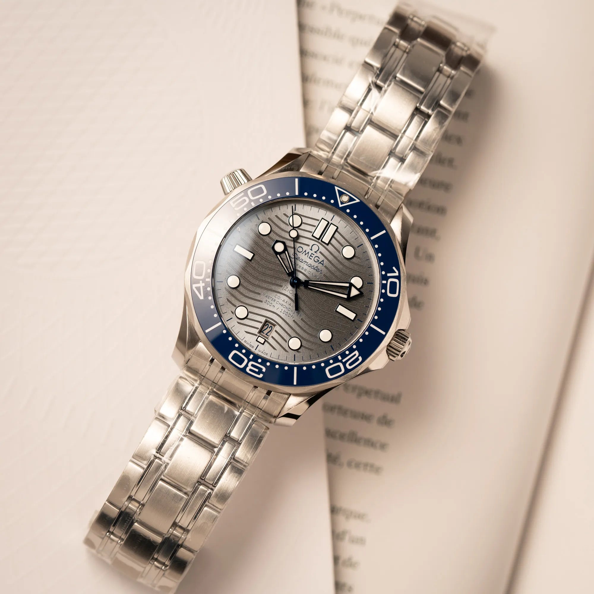Omega Seamaster Diver 300M der Referenz 210.30.42.20.06.001 mit grauem Zifferblatt im Wellen-Design und blauer Lünette am Edelstahlarmband, welches zum Schutz verklebt wurde