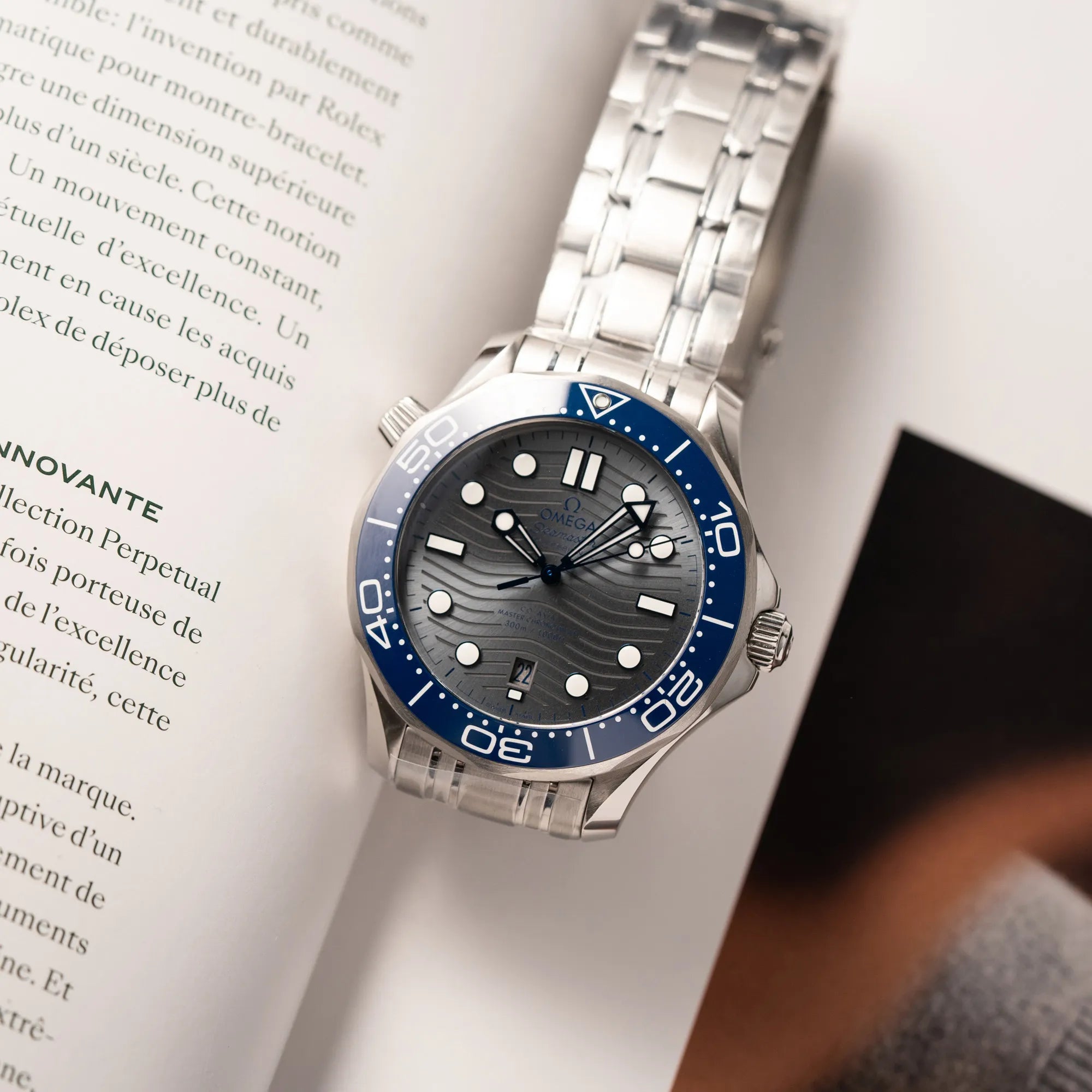 Omega Seamaster Diver 300M der Referenz 210.30.42.20.06.001 mit grauem Zifferblatt im Wellen-Design und blauer Lünette am Edelstahlarmband, welches zum Schutz verklebt wurde