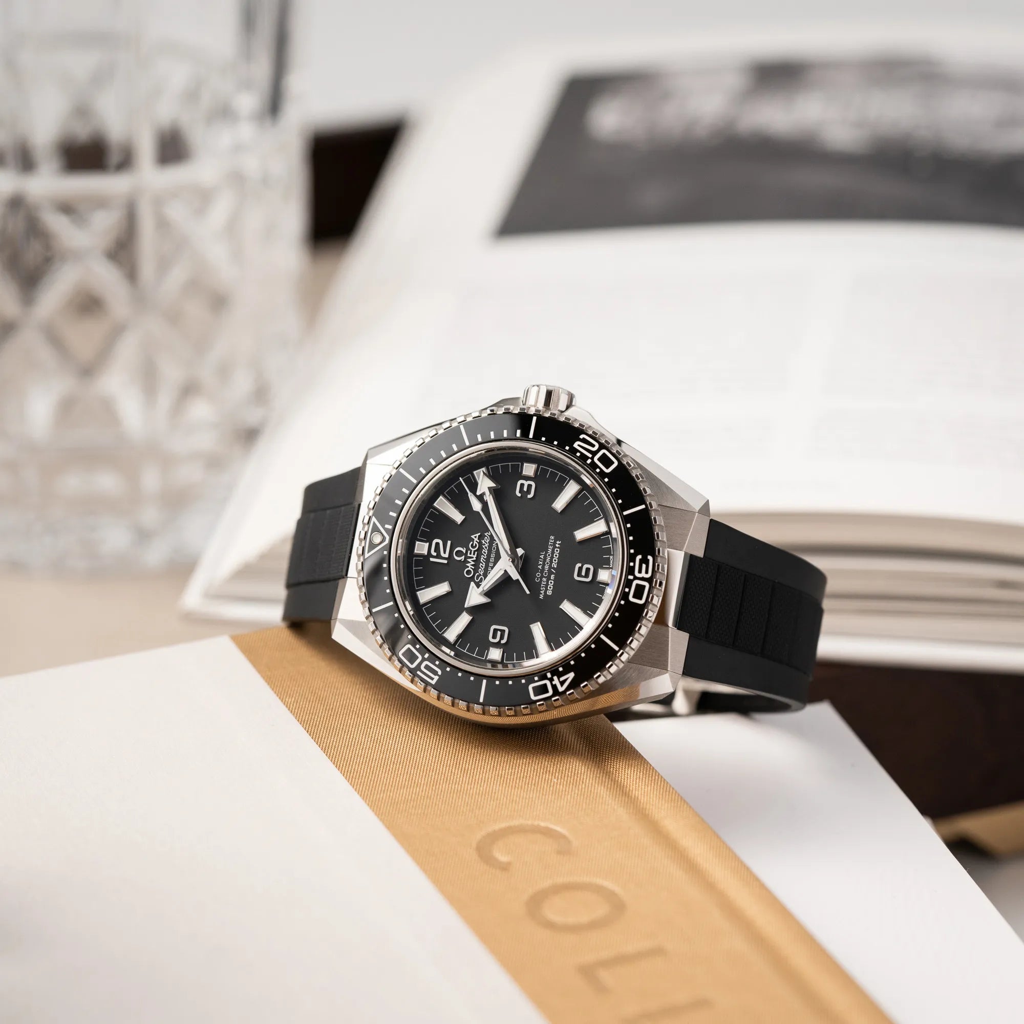 Produktfotografie zeigt die Omega Seamaster Planet Ocean der Referenz 217.32.42.21.01.001 (4. Generation) mit schwarzem Zifferblatt und Lünette am schwarzen Kautschuk-Armband, während die Uhr auf einem Buch liegt