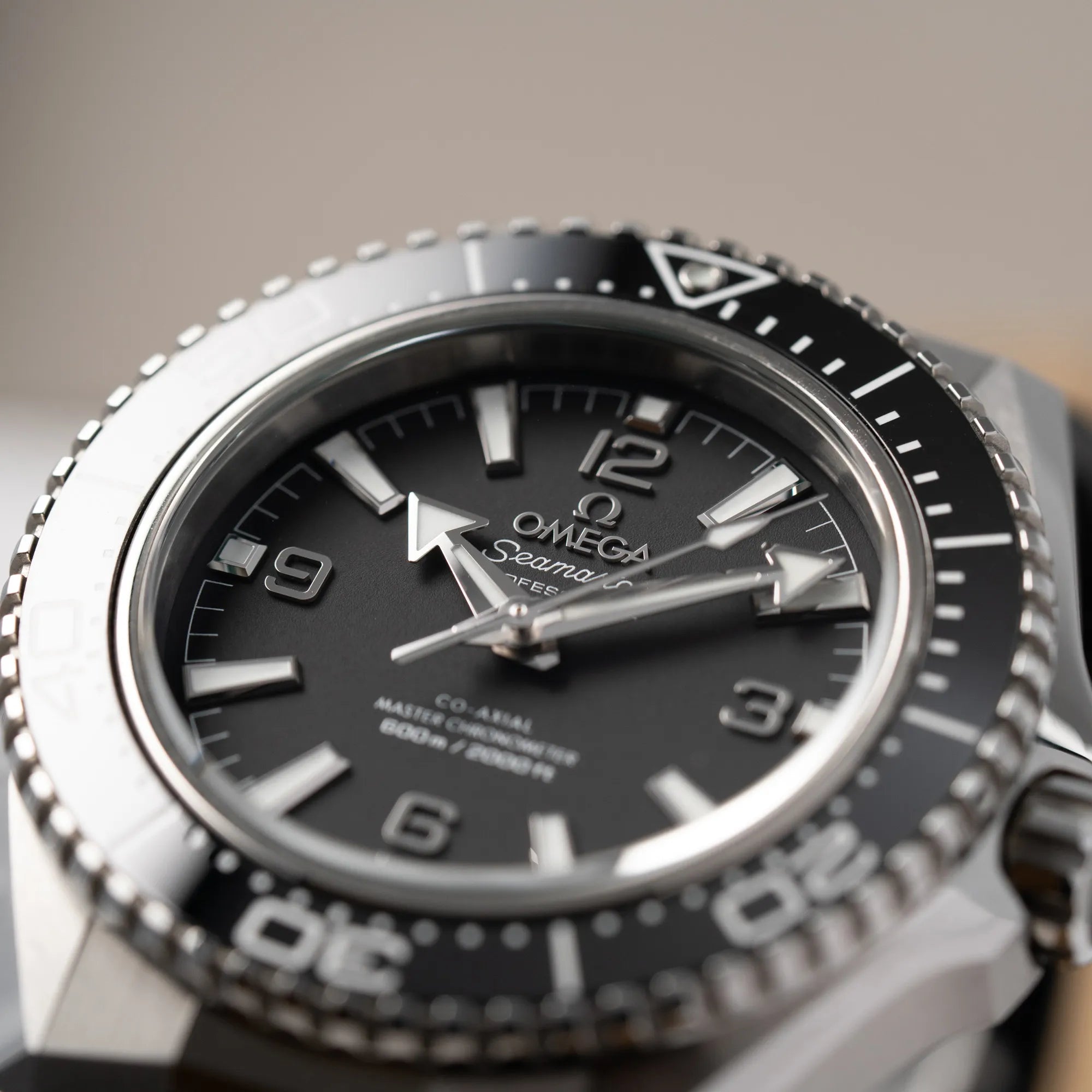 Produktfotografie der Omega Seamaster Planet Ocean der Referenz 217.32.42.21.01.001 (4. Generation) mit schwarzem Zifferblatt und Lünette am schwarzen Kautschuk-Armband mit Fokus auf dem 9-Uhr-Index aus Edelstahl