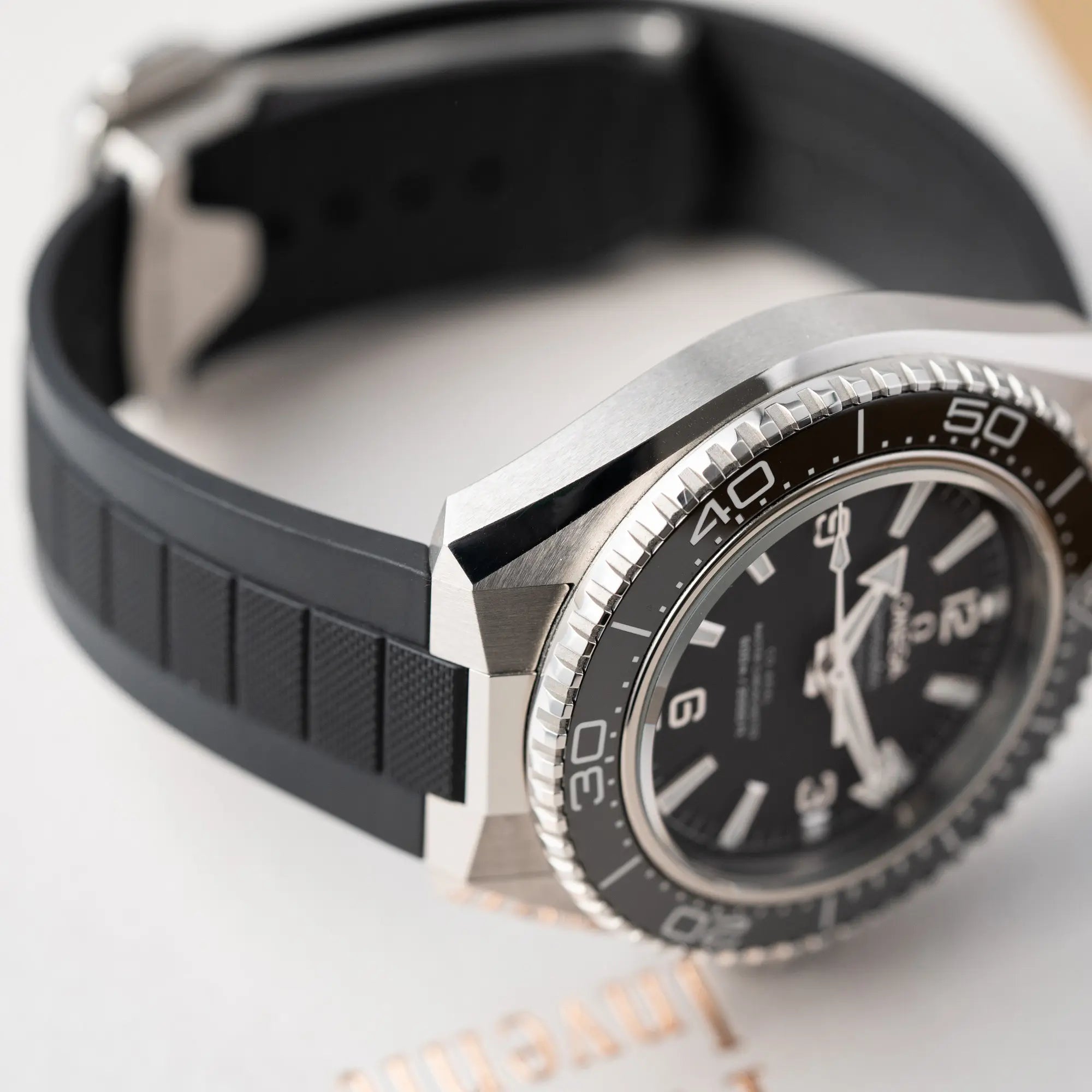 Produktfotografie der Omega Seamaster Planet Ocean der Referenz 217.32.42.21.01.001 (4. Generation) mit schwarzem Zifferblatt und Lünette am schwarzen Kautschuk-Armband zeigt die Lünette und den kantigen Bandanstoß