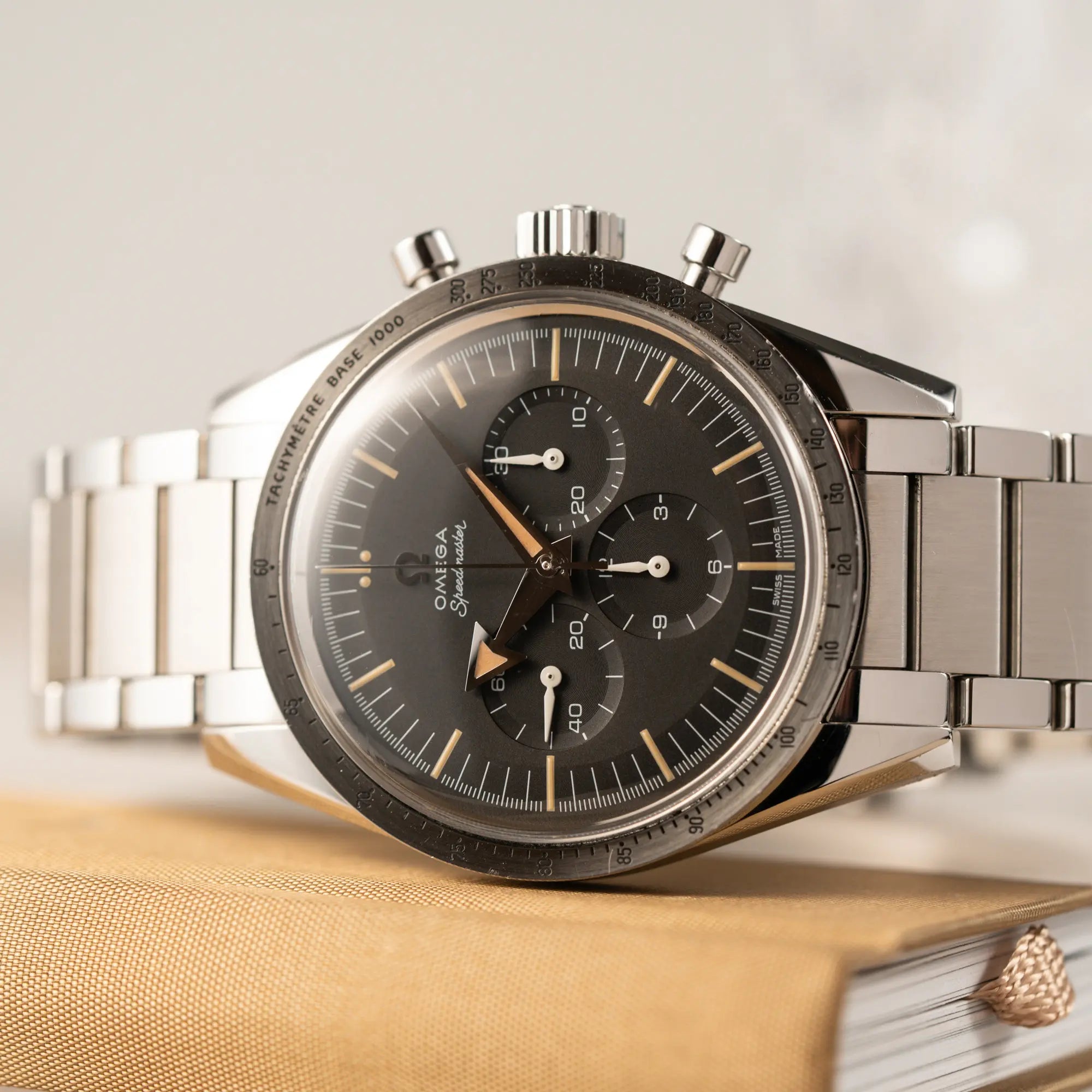 Detailaufnahme der seitlich auf dem Uhrengehäuse liegenden Omega Speedmaster 1957 Trilogy Limited Edition mit einem anthrazitfarbenen Zifferblatt mit Vintage-Look und dem original Omega-Stahlband im Ed-White-Design