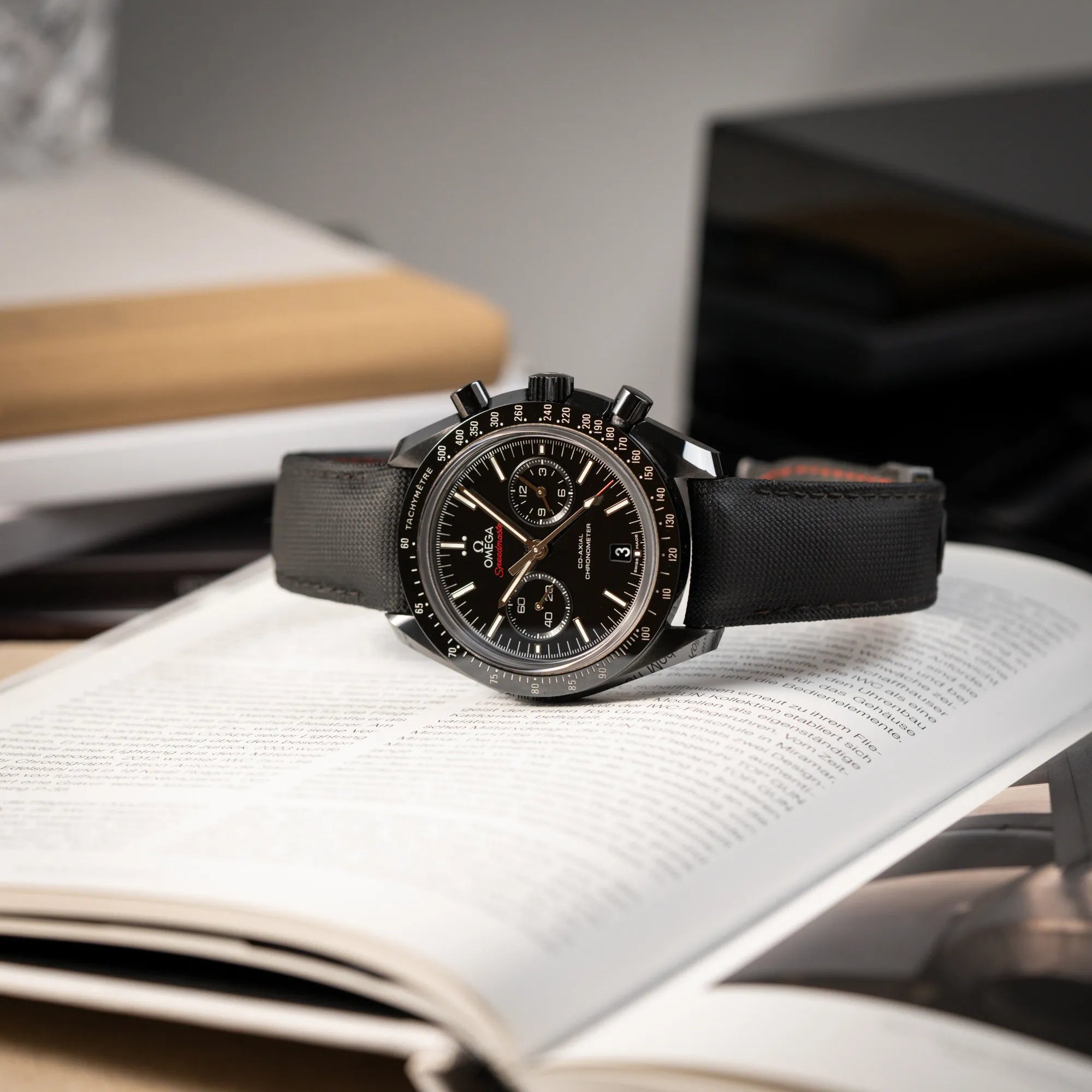 Produktfotografie des Omega Speedmaster "Darkside of the Moon" Chronograph mit schwarzem Zifferblatt und aus schwarzer Keramik gefertigtem Gehäuse, während die Uhr auf dem seitlichen Gehäuse liegt