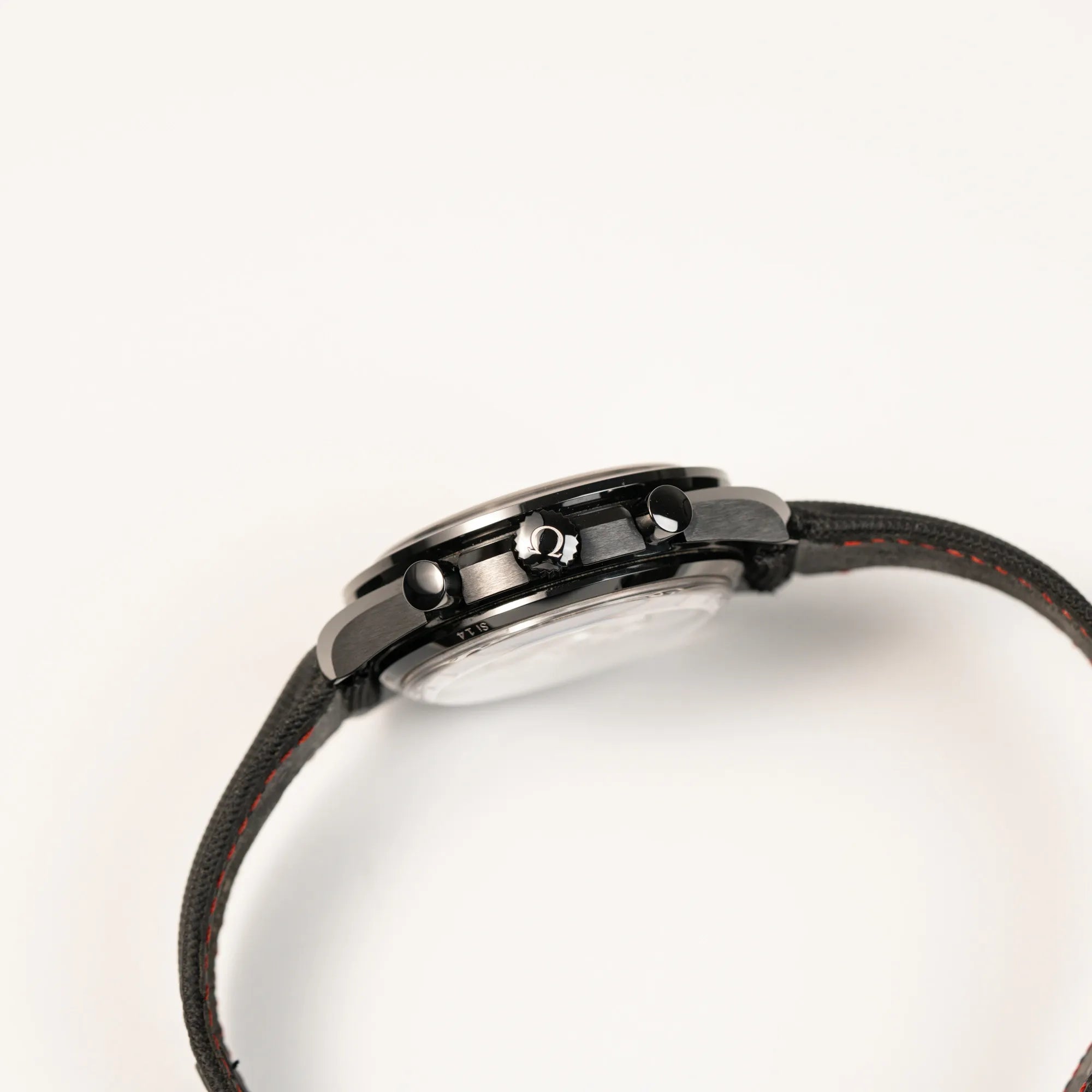 Seitliche Gehäuseflanke von dem Omega Speedmaster "Darkside of the Moon" Chronograph mit schwarzem Zifferblatt und aus schwarzer Keramik gefertigtem Gehäuse zeigt die Aufzugskrone mit Omega-Logo und die Chronograph-Drücker