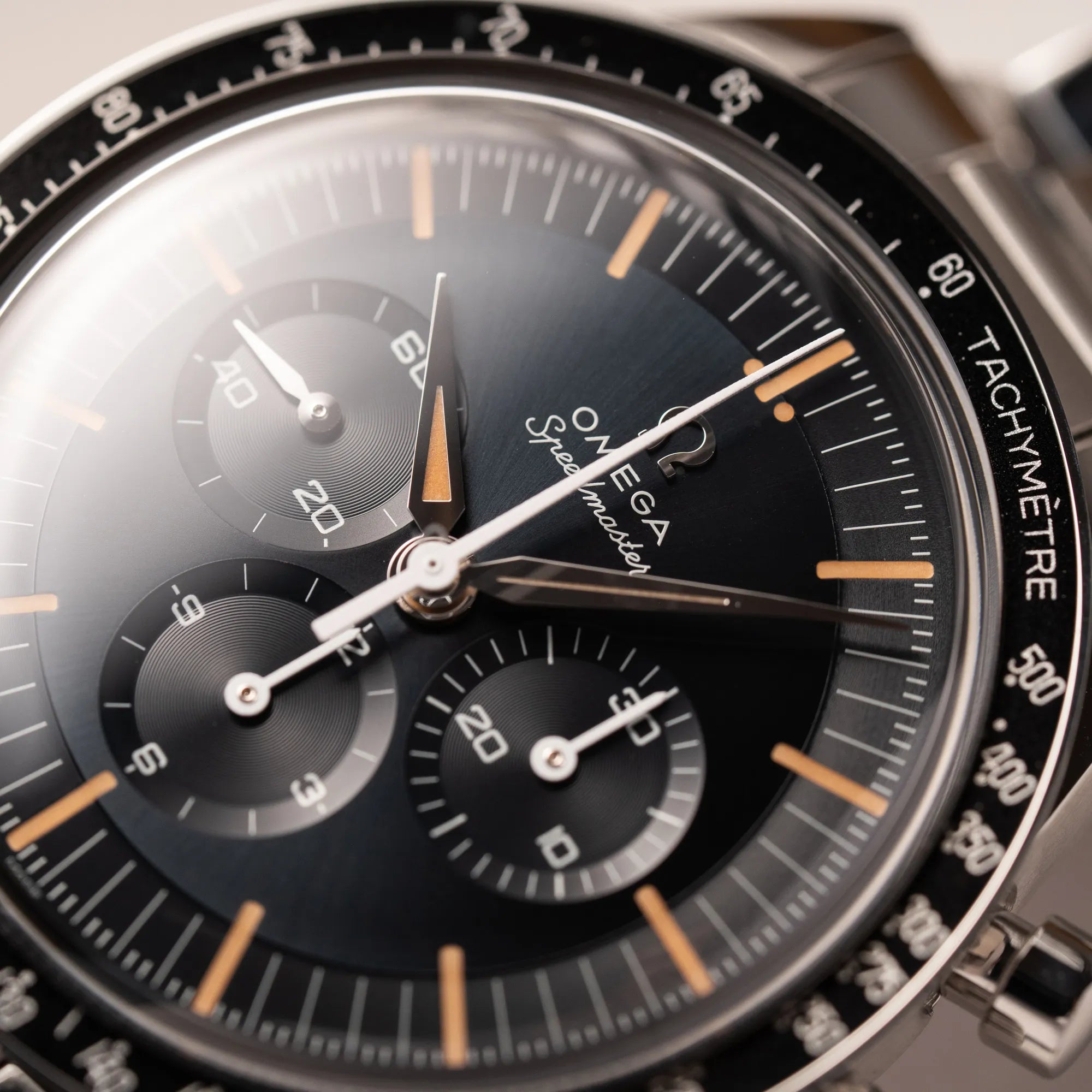 Detailaufnahme mit Fokus auf dem Zeigersatz von der Omega Speedmaster FOIS der Referenz 310.30.40.50.06.001 mit dem dunkelblauen Zifferblatt mit dunkel-beigen Indizes im Vintage-Look und einem vom Standard-Modell abgeänderten Stahl-Armband, was beides an das klassische Speedy-Modell erinnert