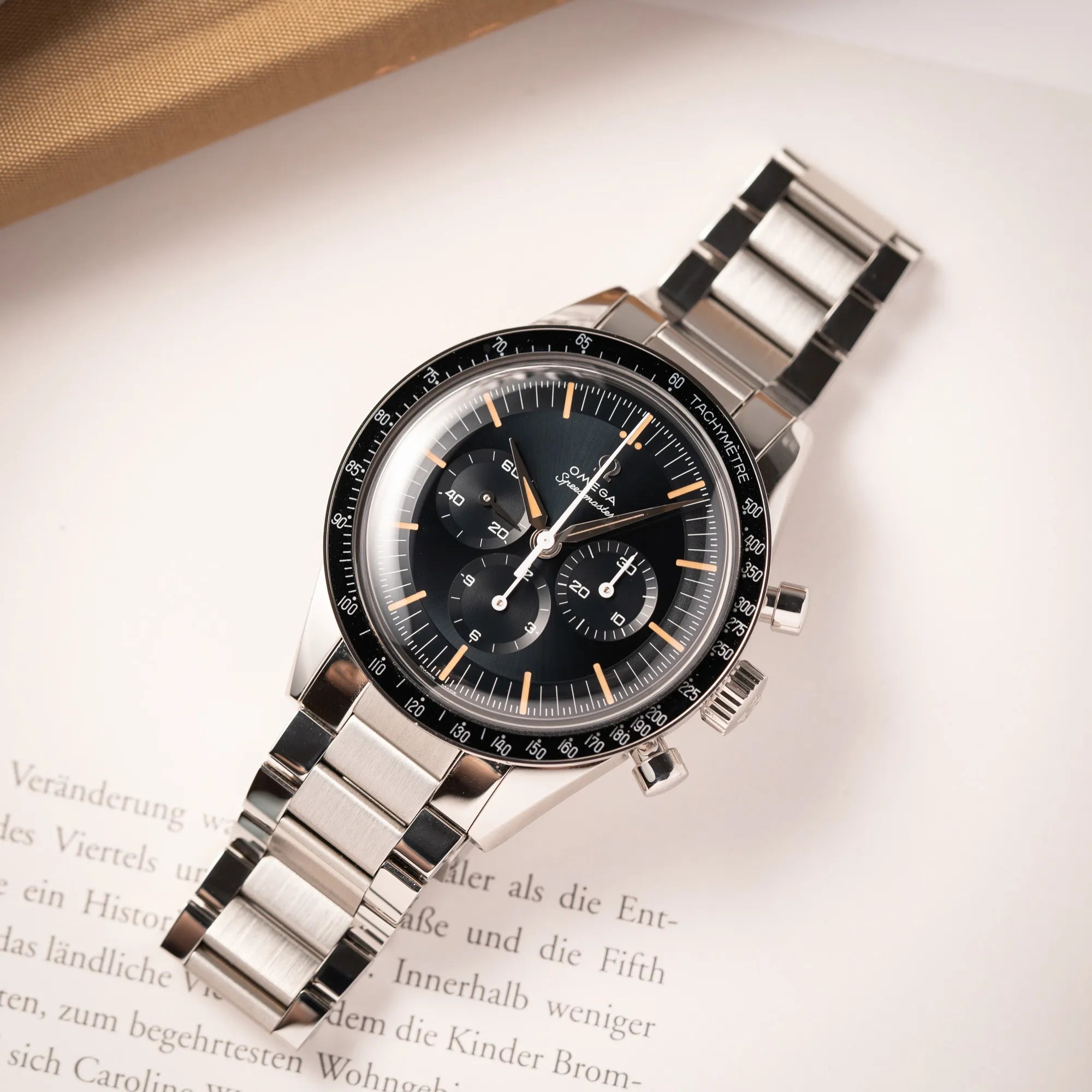 Produktfotografie aus der Vogelperspektive zeigt die Omega Speedmaster FOIS der Referenz 310.30.40.50.06.001 mit dem dunkelblauen Zifferblatt mit dunkel-beigen Indizes im Vintage-Look und einem vom Standard-Modell abgeänderten Stahl-Armband, was beides an das klassische Speedy-Modell erinnert