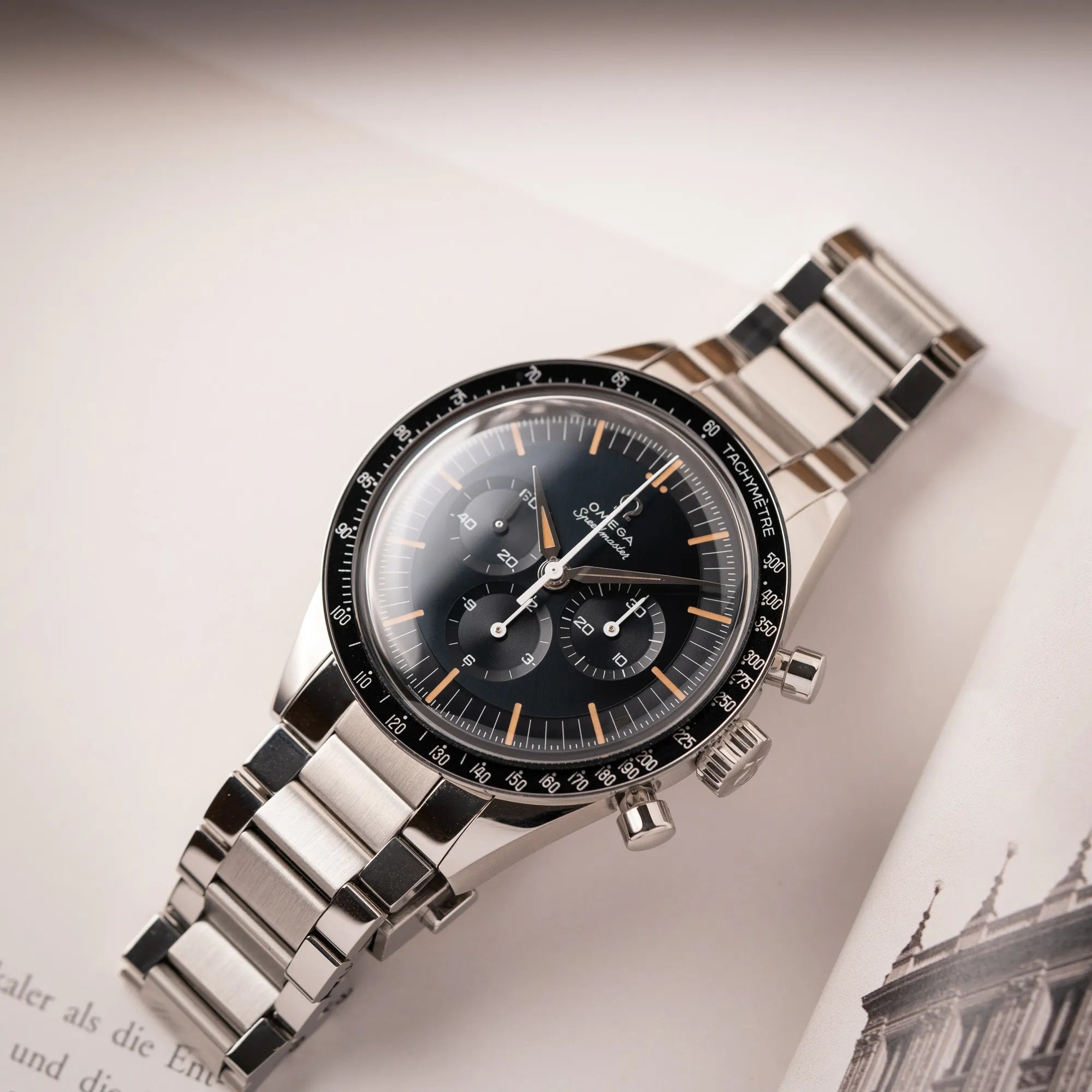 Produktfotografie als Titelbild für die Omega Speedmaster FOIS der Referenz 310.30.40.50.06.001 mit dem dunkelblauen Zifferblatt mit dunkel-beigen Indizes im Vintage-Look und einem vom Standard-Modell abgeänderten Stahl-Armband, was beides an das klassische Speedy-Modell  erinnert