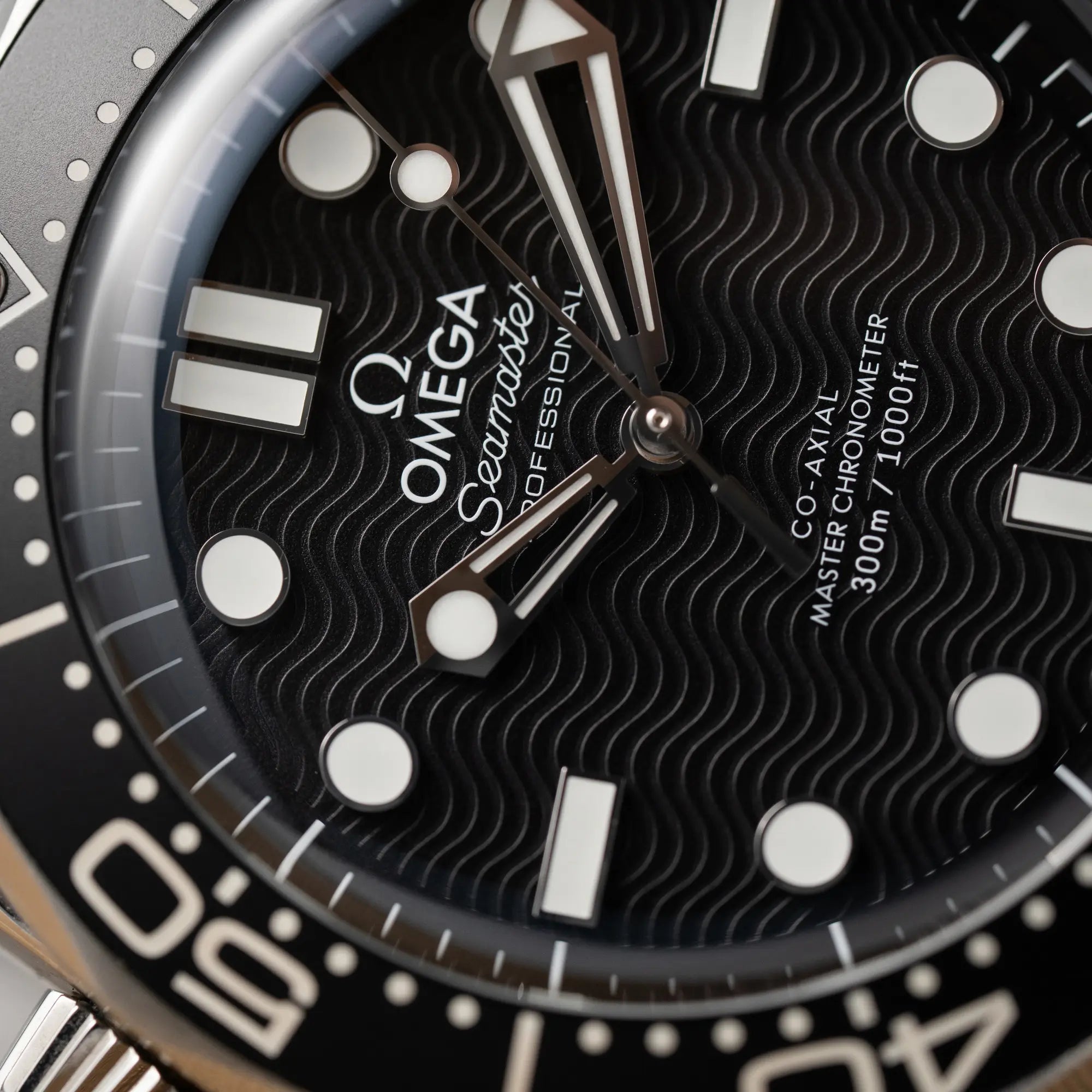 Makroaufnahme zeigt die Struktur des schwarzen Zifferblatt, dessen Design passend für eine Taucheruhr an Wellen erinnert, von der Omega Seamaster 300M Diver 210.30.42.20.01.010