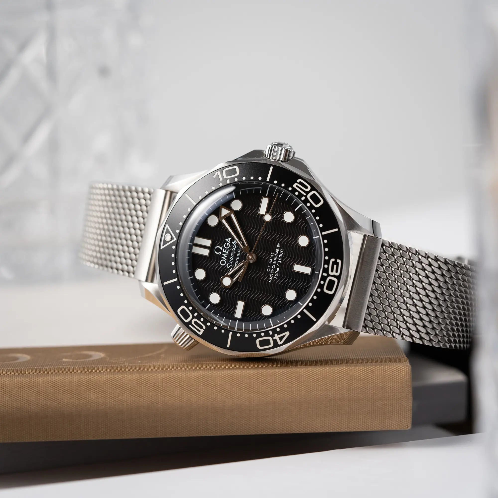 Produktfotografie der seitlich auf dem Uhrengehäuse liegenden Omega Seamaster 300M Diver 210.30.42.20.01.010 mit dems schwarzen Zifferblatt im Wellen-Design am Milanese-Edelstahl-Armband