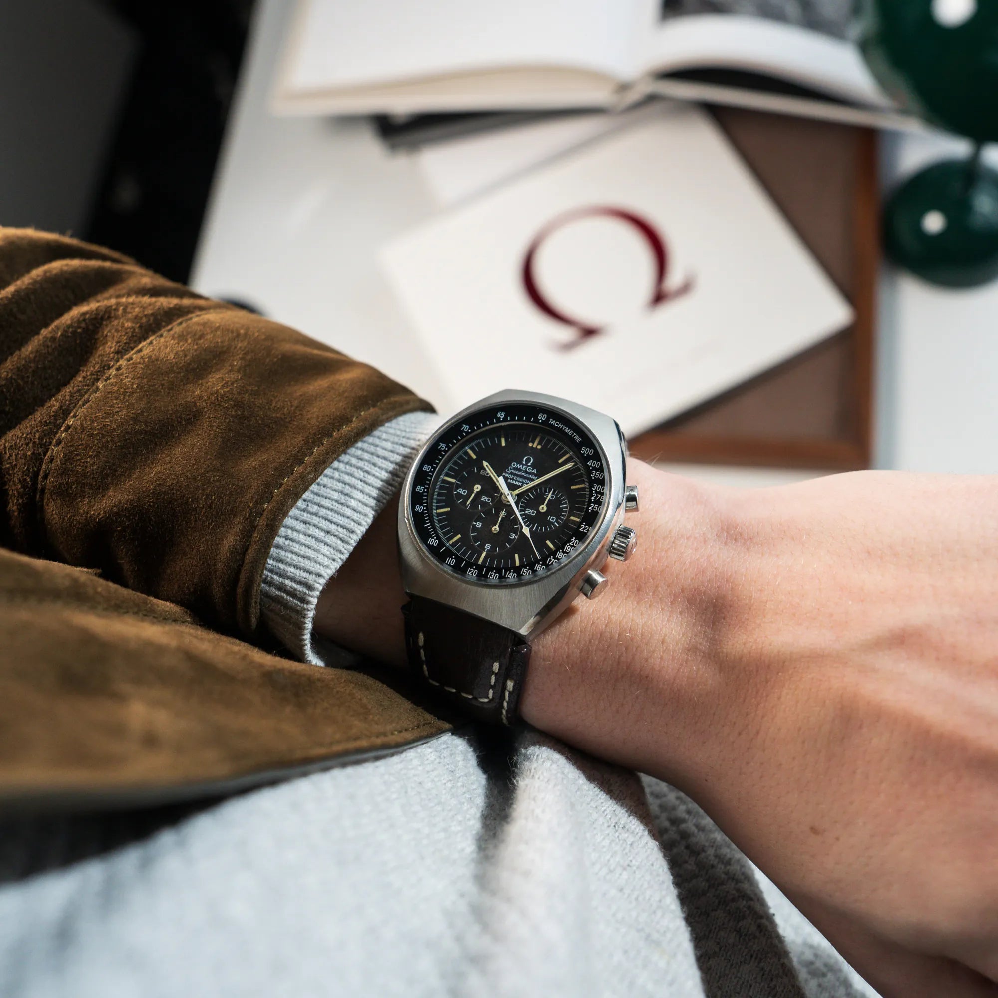 Mann trägt die Produktfotografie der liegenden Omega Speedmaster Moonwatch Mark 2 an einem braunen Lederarmband an seinem Handgelenk und präsentiert diese