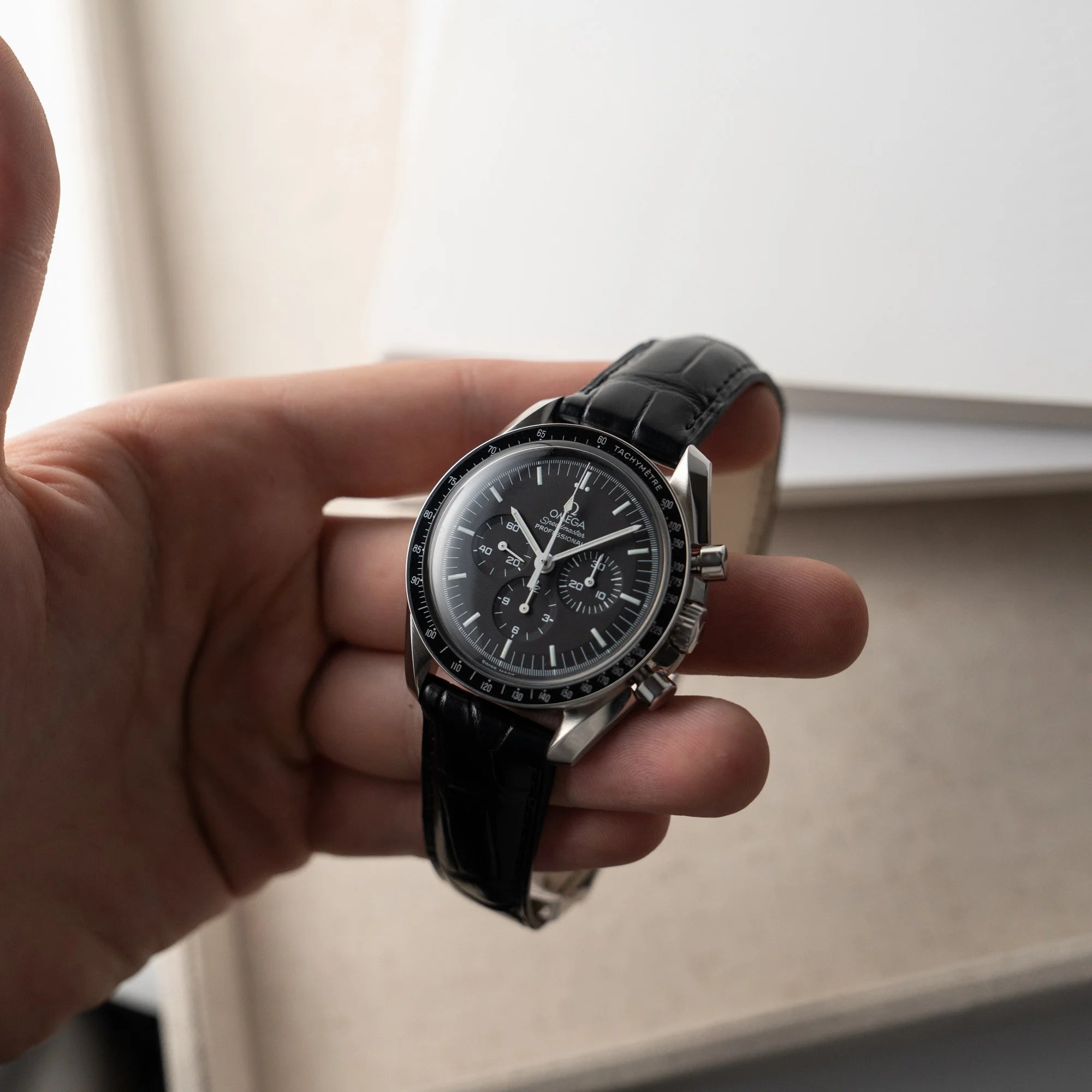 Mann hält die Omega Speedmaster Moonwatch Professional am schwarzen Lederband in seiner Hand und präsentiert die Armbanduhr in die Kamera