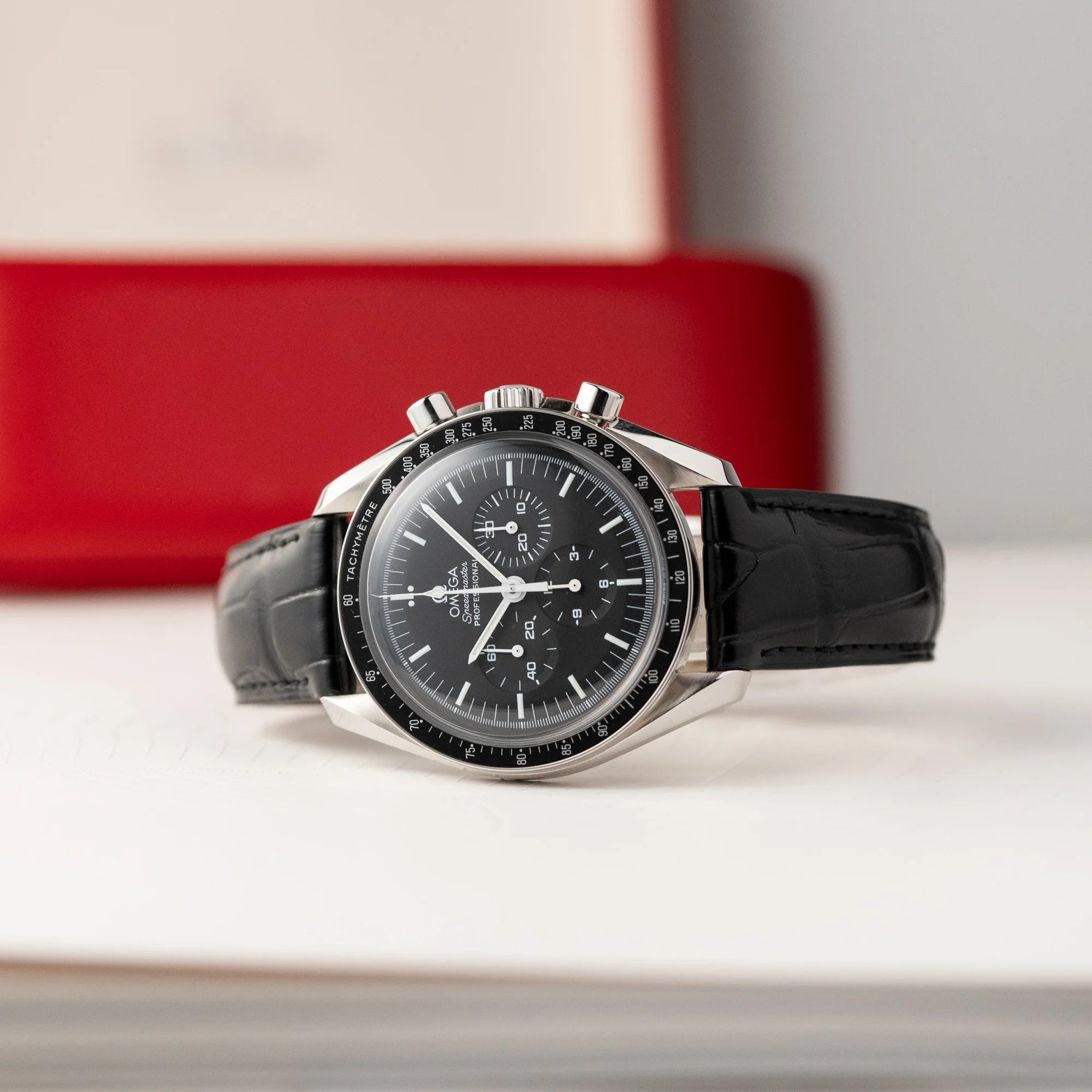 Produktfotografie der seitlich liegenden Omega Speedmaster Moonwatch Professional am schwarzen Lederband