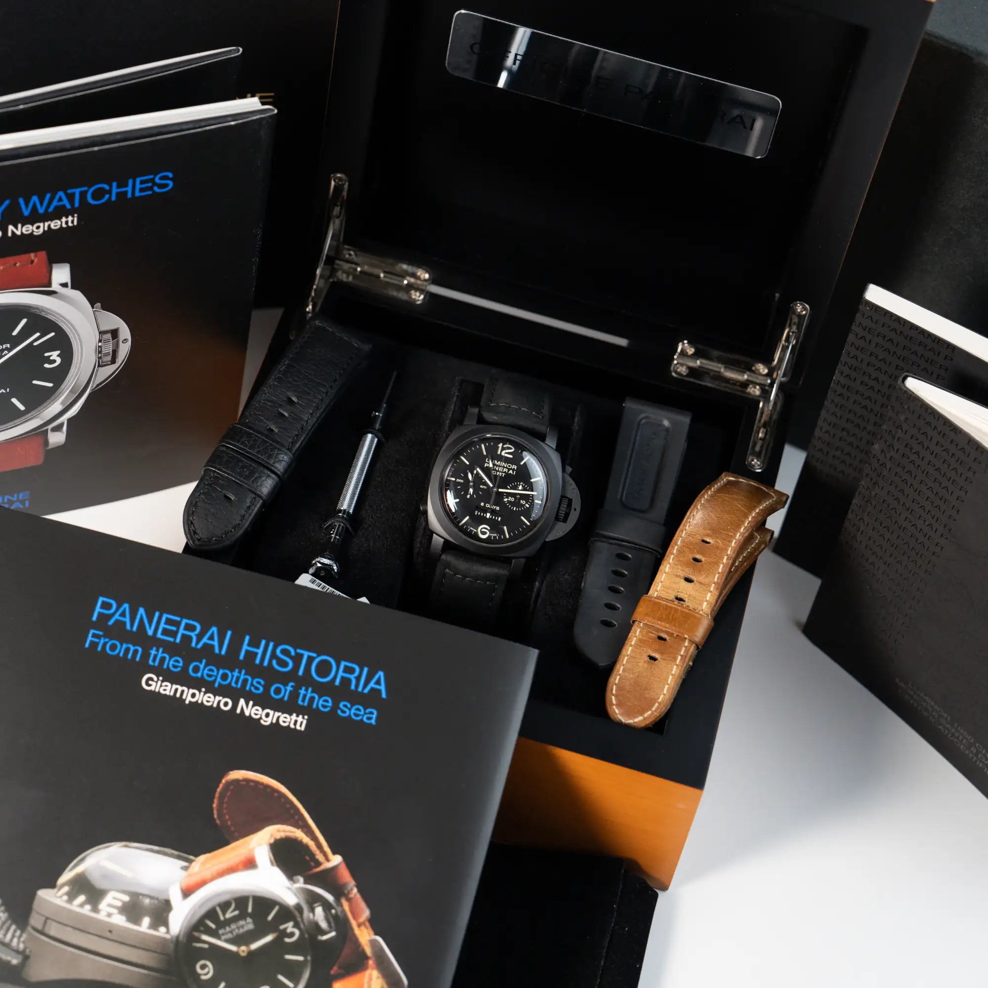 Produktfotografie der Panerai Luminor Monupulsante 8 Days mit schwarzem Keramik-Gehäuse mit creme-weißen Indizes zusammen mit dem Lieferumfang als Full-Set