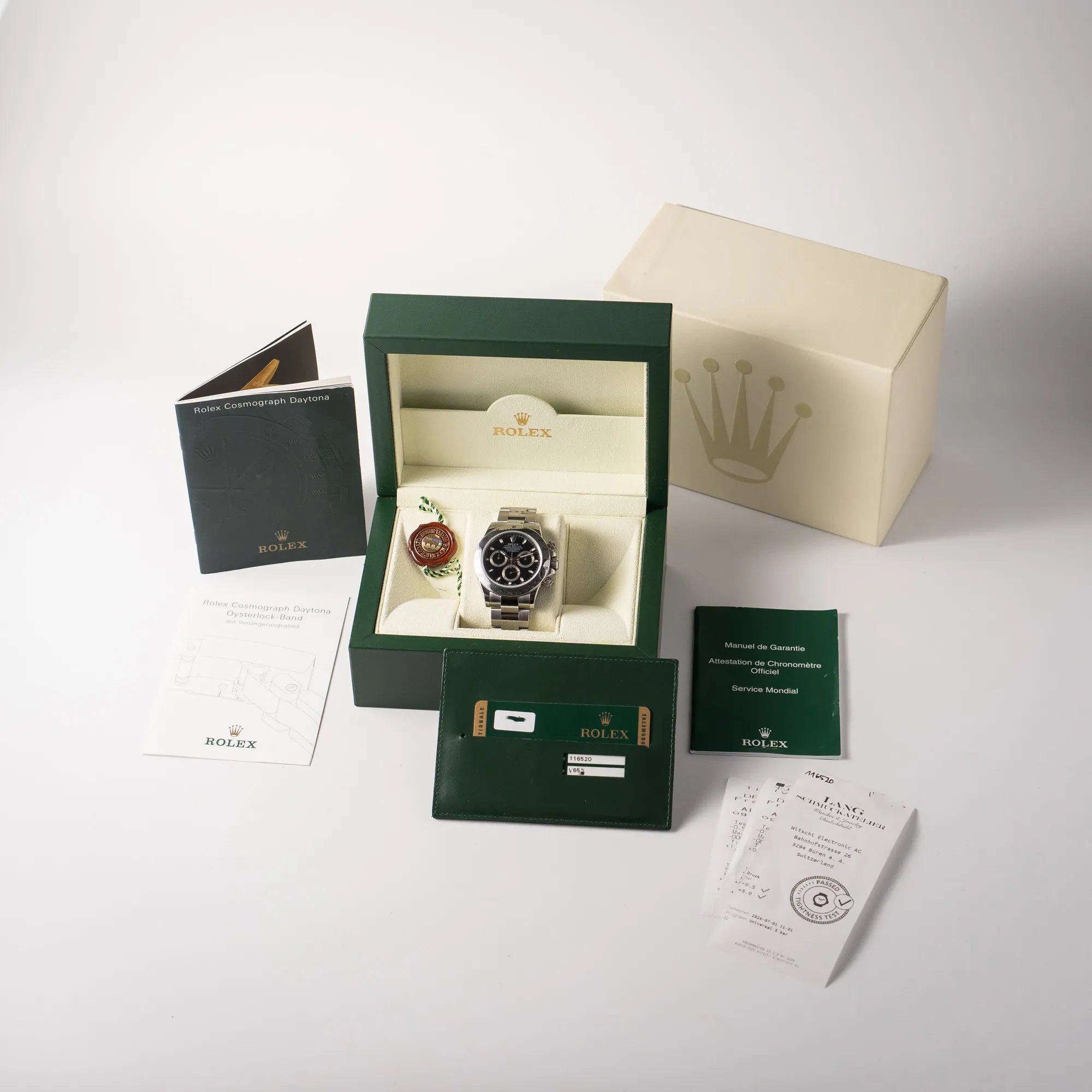 Lieferumfang zu der Rolex Cosmograph Daytona 116520 mit schwarzem Zifferblatt und der klassischen Edelstahl-Lünette vor Umstellung auf die Keramik-Lünette aus 2009, bestehend aus Box mit Ukarton, originaler Garantiekarte, Booklets, Dichtheitstest und Hangtag