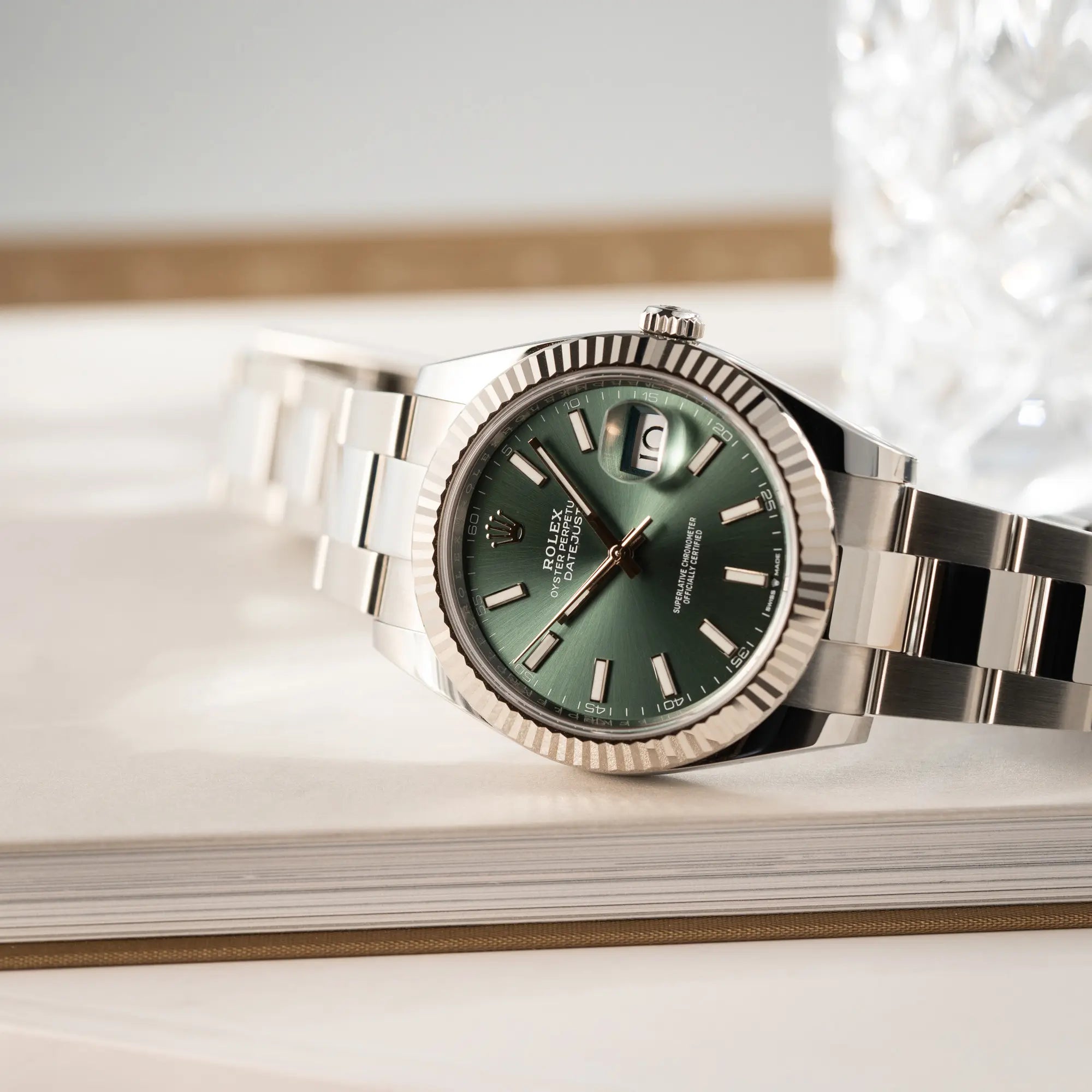 Produktfotografie der seitlich auf dem Uhrengehäuse liegenden Rolex Datejust 41 der Referenz 126334 mit dem grünem Zifferblatt am Oyster-Stahlband