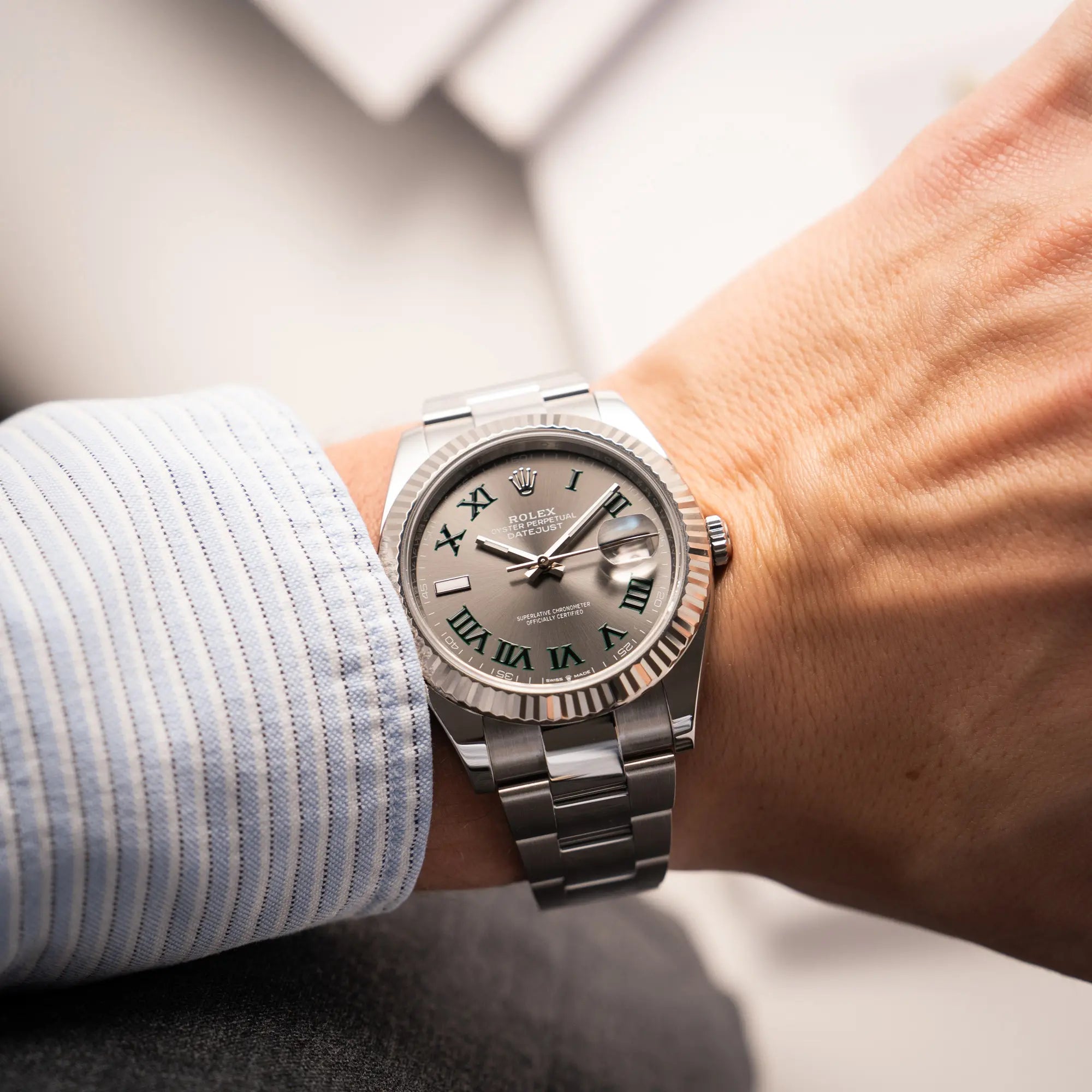 Mann trägt die Rolex Datejust 41 der Referenz 126334 mit geriffelter Weißgold-Lünette und Oyster-Stahlband mit dem grauen Wimbledon-Zifferblatt mit schwarz-grünen Indizes an seinem Handgelenk