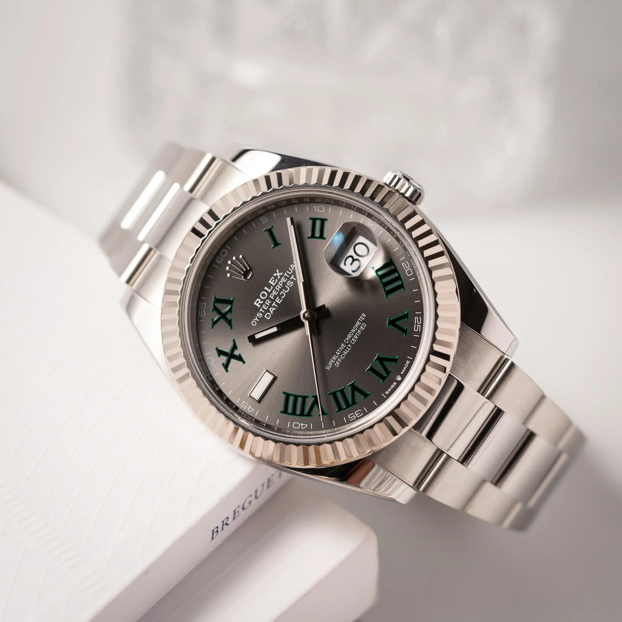 Produktfotografie der Rolex Datejust 41 der Referenz 126334 mit geriffelter Weißgold-Lünette und Oyster-Stahlband mit dem grauen Wimbledon-Zifferblatt mit schwarz-grünen Indizes