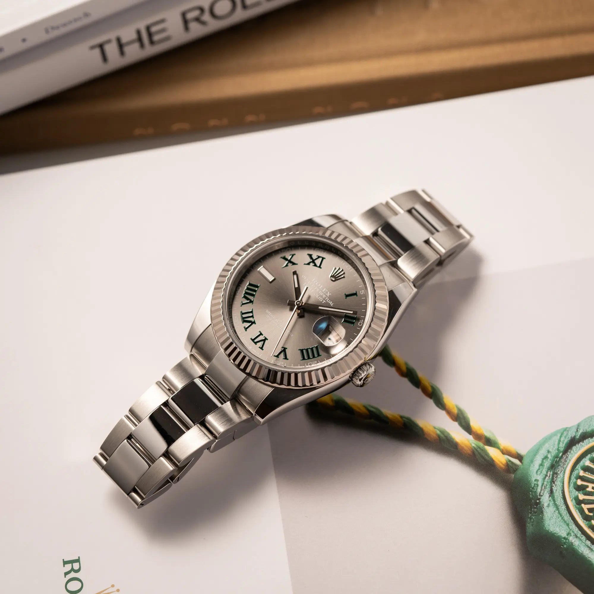 Rolex Datejust 41 der Referenz 126334 mit geriffelter Weißgold-Lünette und Oyster-Stahlband mit dem grauen Wimbledon-Zifferblatt mit schwarz-grünen Indizes liegt flach auf einem Buch über Rolex-Uhren