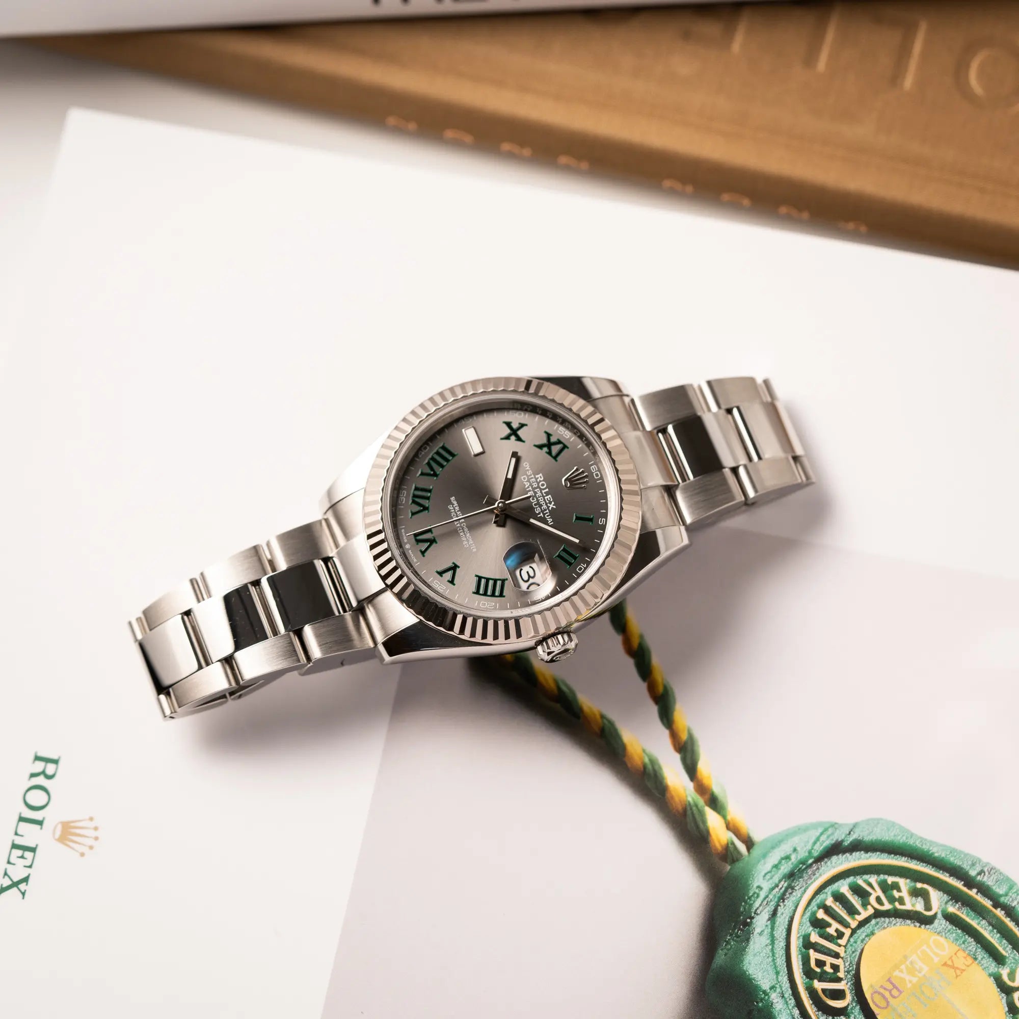 Rolex Datejust 41 der Referenz 126334 mit geriffelter Weißgold-Lünette und Oyster-Stahlband mit dem grauen Wimbledon-Zifferblatt mit schwarz-grünen Indizes liegt flach auf einem Buch über Rolex Uhren