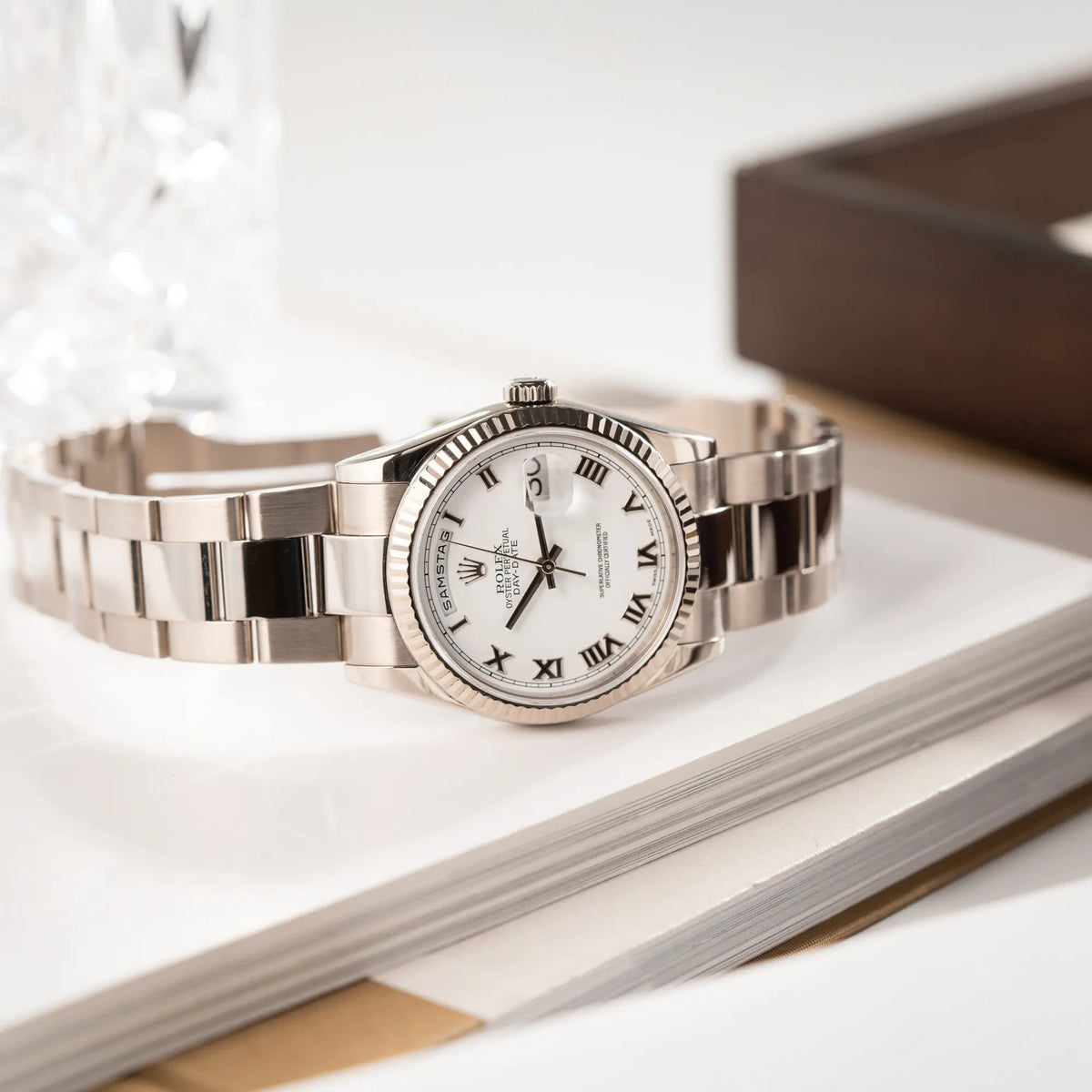 Produktfotografie der seitlich auf dem Uhrengehäuse liegenden Rolex Day-Date 36 Armbanduhr in Weißgold der Referenz 118239 mit weißem Zifferblatt mit römischen Indizes am Oyster-Weißgold-Armband