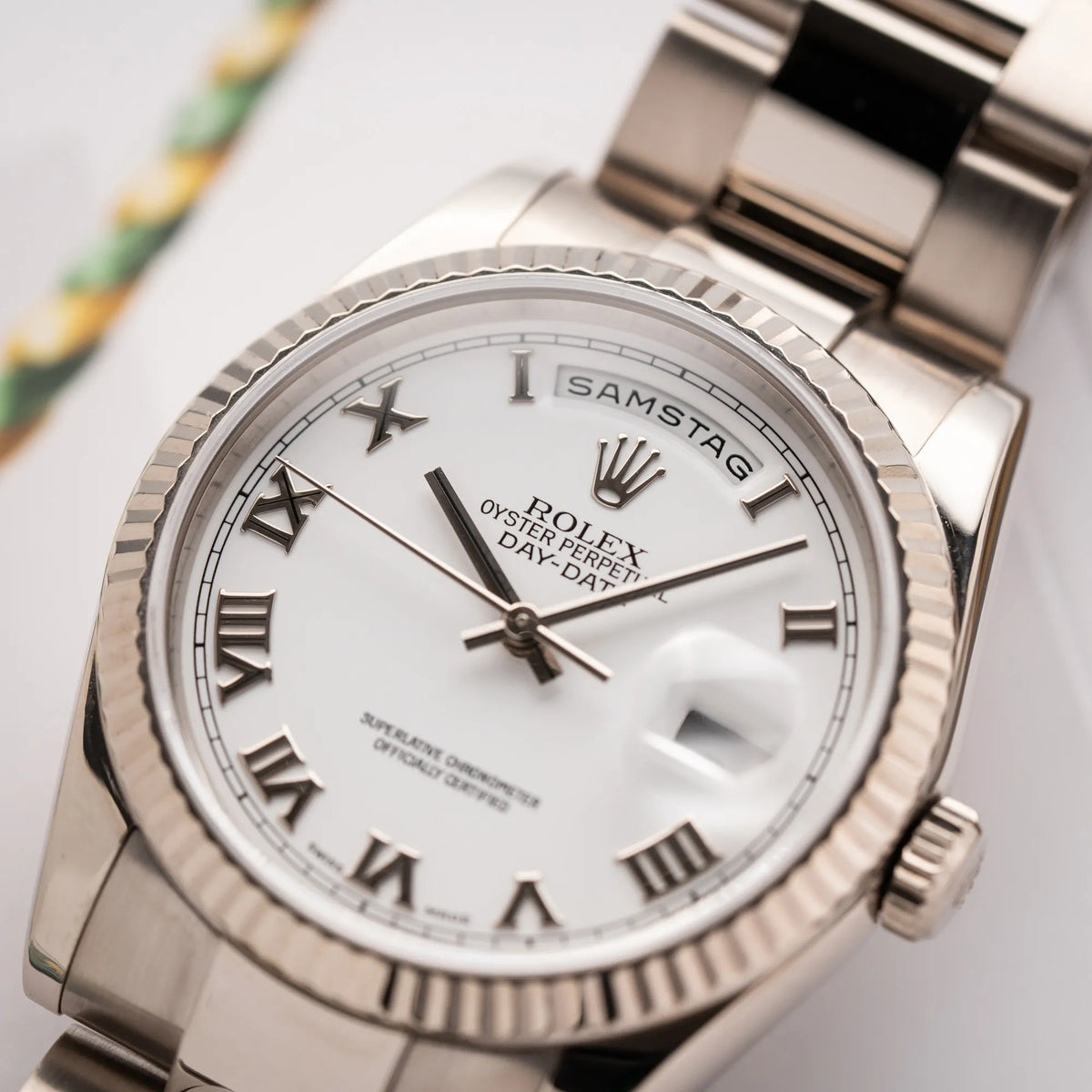 Detailaufnahme der Rolex Day-Date 36 Armbanduhr in Weißgold der Referenz 118239 mit weißem Zifferblatt mit römischen Indizes am Oyster-Weißgold-Armband mit Fokus auf der Wochentagsanzeige bei 12 Uhr, die gerade Samstag anzeigt