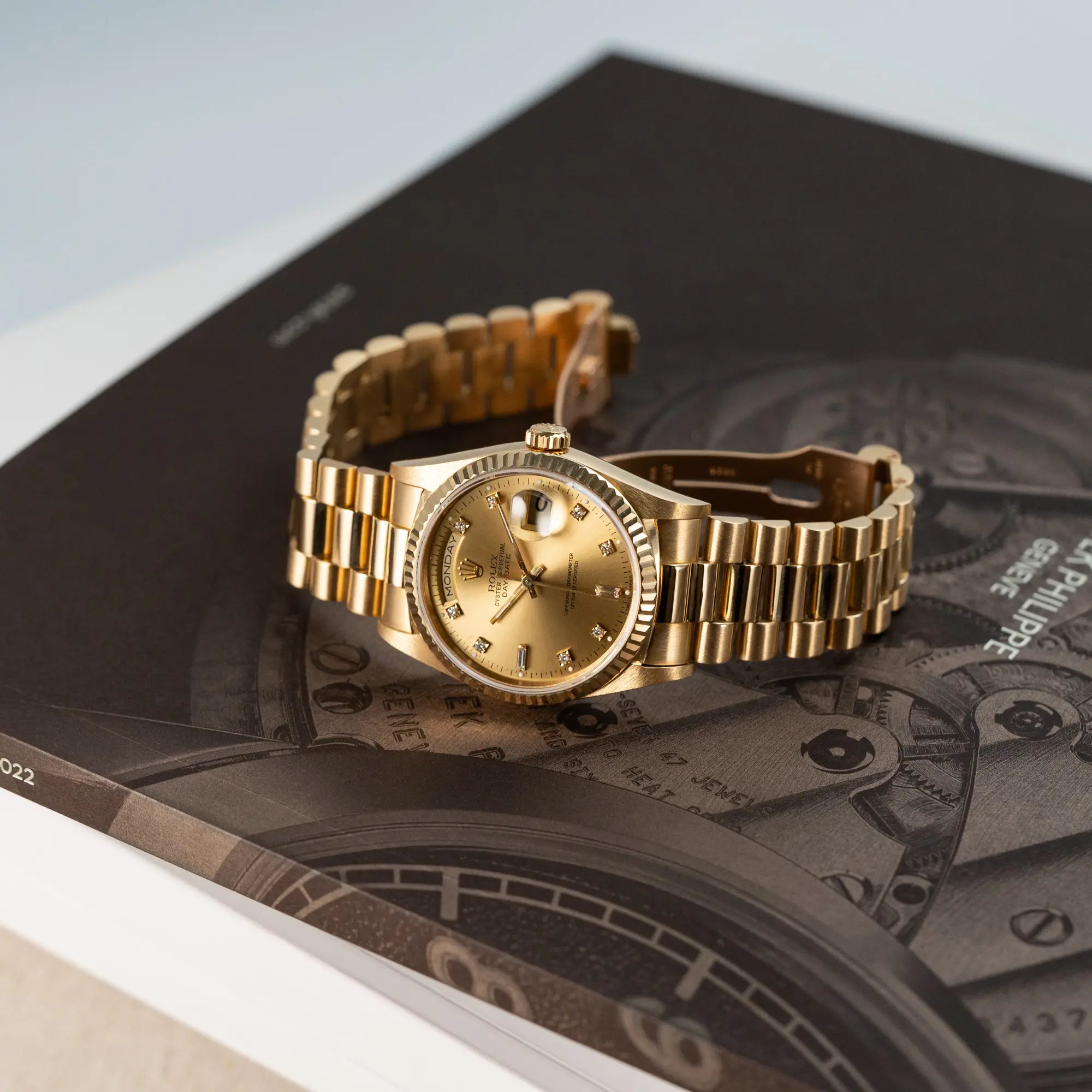 Produktfotografie der seitlich auf dem Gehäuse liegenden Rolex Day-Date 18238 in Gelbgold mit goldenem Zifferblatt und Diamant-Indizes am President-Armband