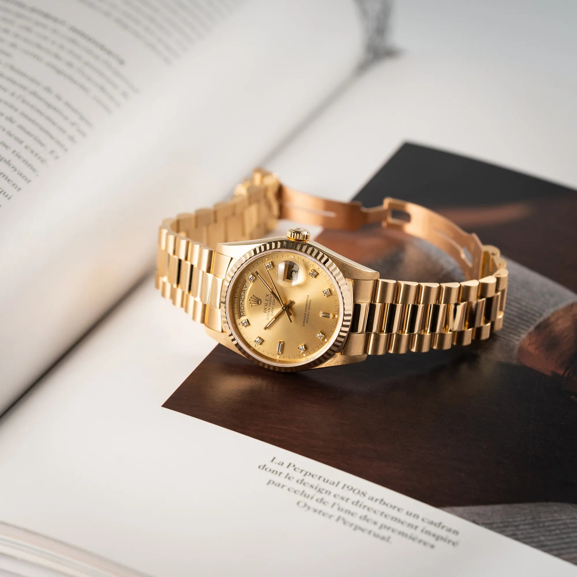 Rolex Day-Date 36 in Gelbgold der Referenz 18238 aus 1991 mit Champagner-Diamant-Zifferblatt und englischsprachiger Tagesanzeige liegt mit geöffneter Faltschliesse auf einem Buch