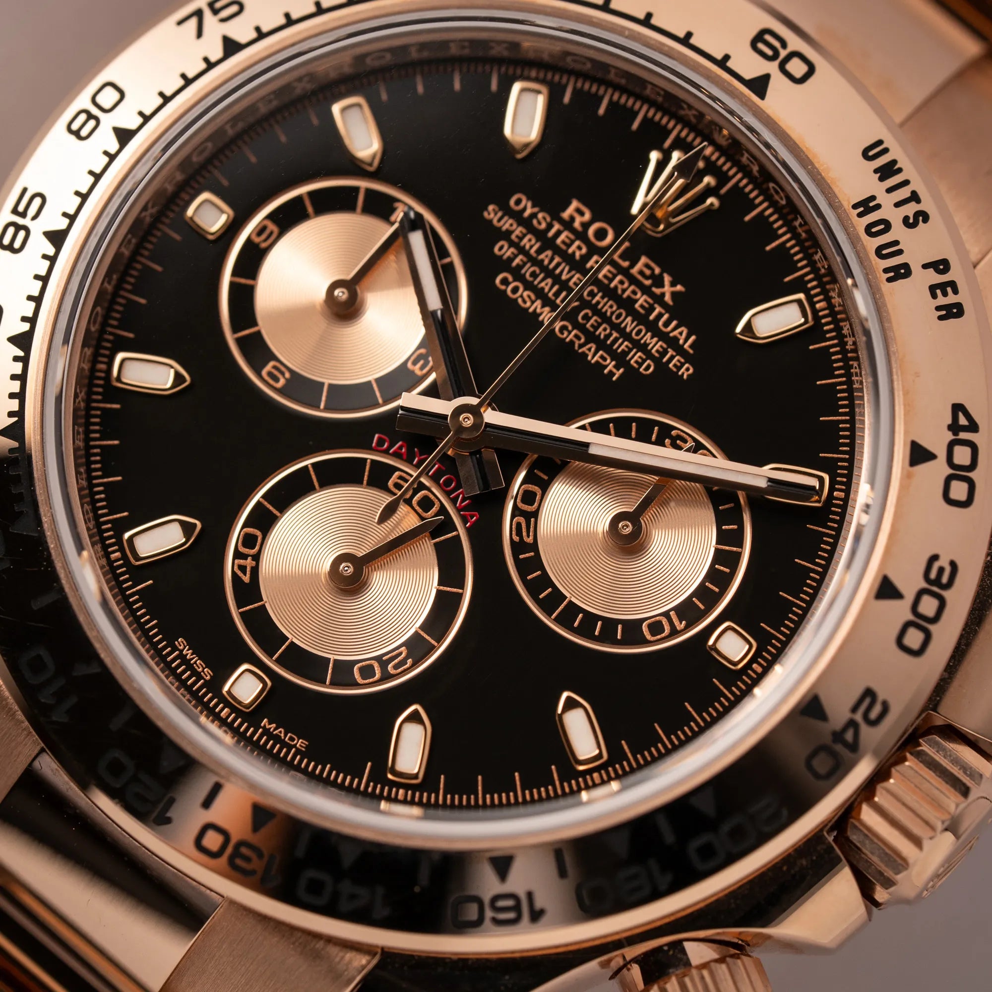 Detailaufnahme des Zifferblatts mit rotem Daytona-Schriftzug und rostgoldenen Sub-Dials von der Rolex Daytona Chronograph-Armbanduhr der Referenz 116505 in Everrose-Roségold mit schwarzem Zifferblatt am Oyster-Roségold-Band