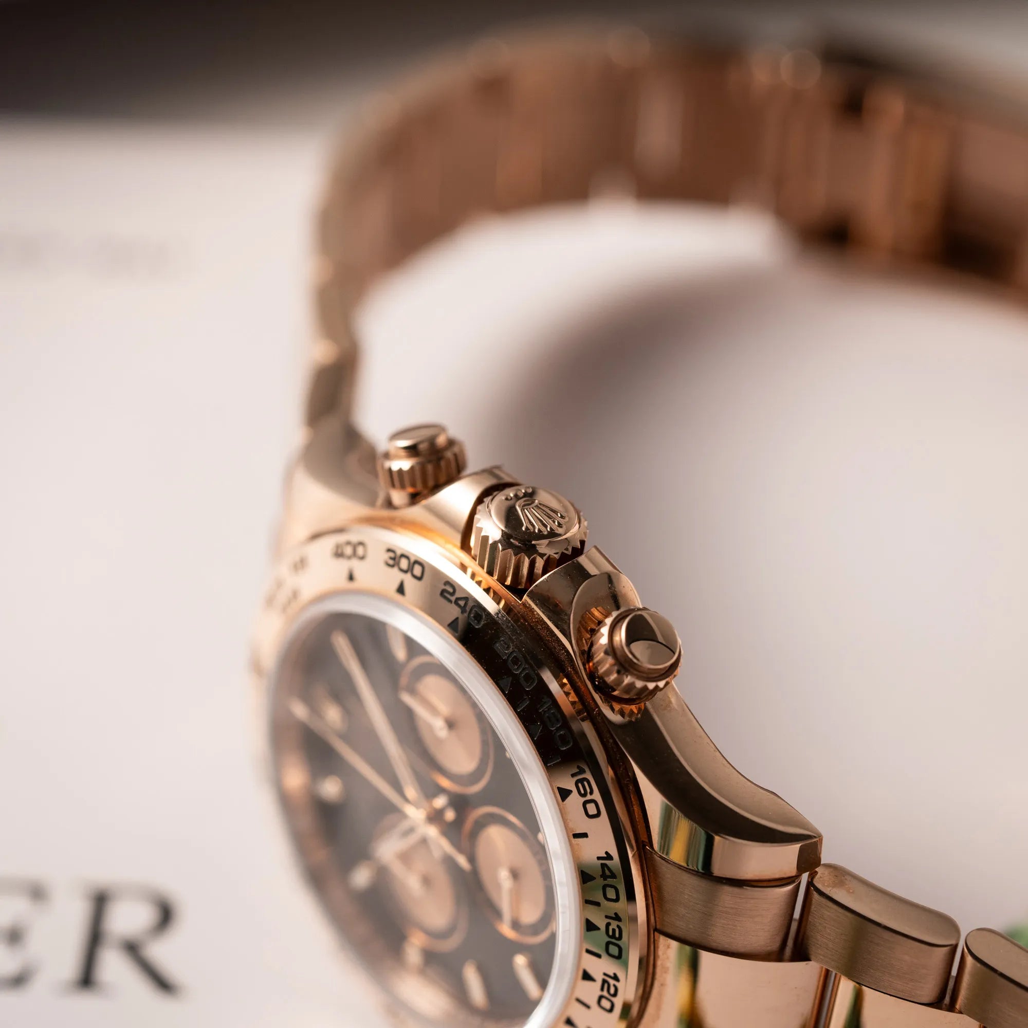 Detailaufnahme der Auzugskrone und Chrono-Pusher der Rolex Daytona Chronograph-Armbanduhr der Referenz 116505 in Everrose-Roségold mit schwarzem Zifferblatt am Oyster-Roségold-Band