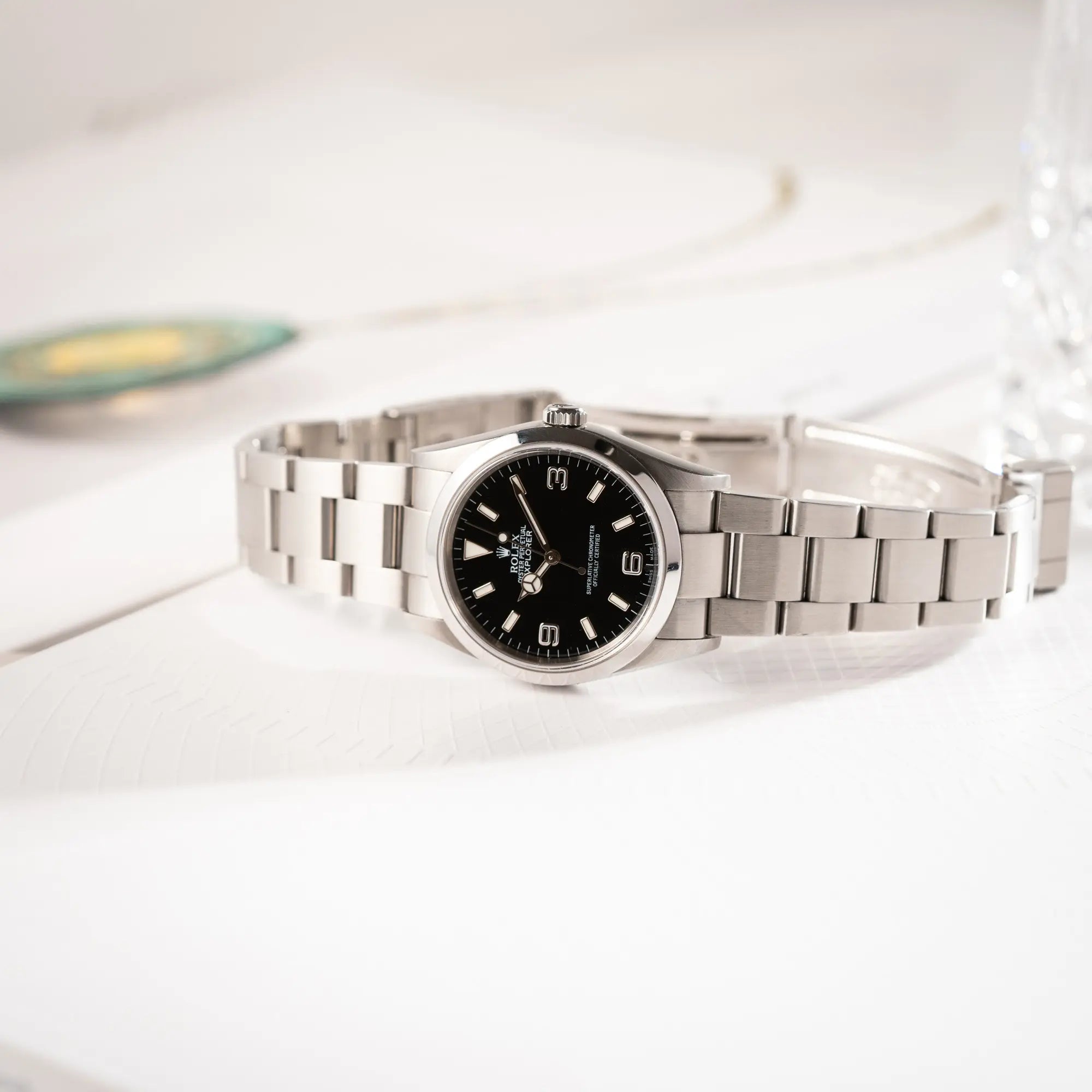 Produktfotografie der seitlich auf dem Uhrengehäuse liegenden Rolex Explorer 36 der Referenz 114270 mit dem klassischen schwarzen 3-6-9-Explorer-Zifferblatt am Oyster-Stahlband mit geöffneter Faltschliesse